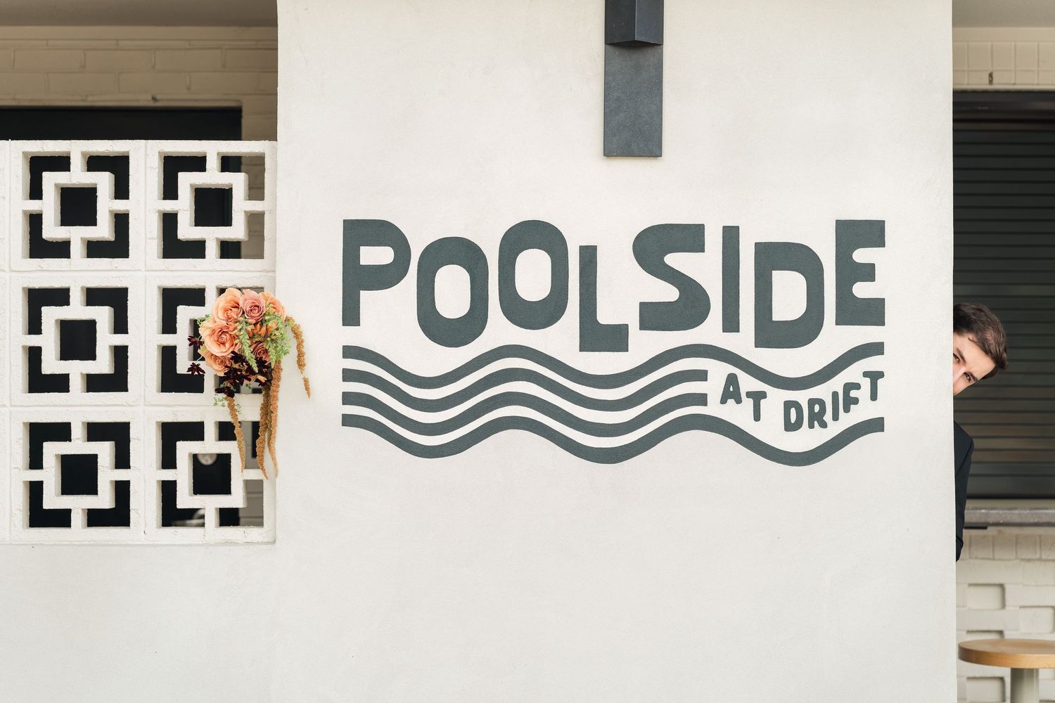 Couple peeking around a white wall with Poolside at Drift sign and geometric window detail.