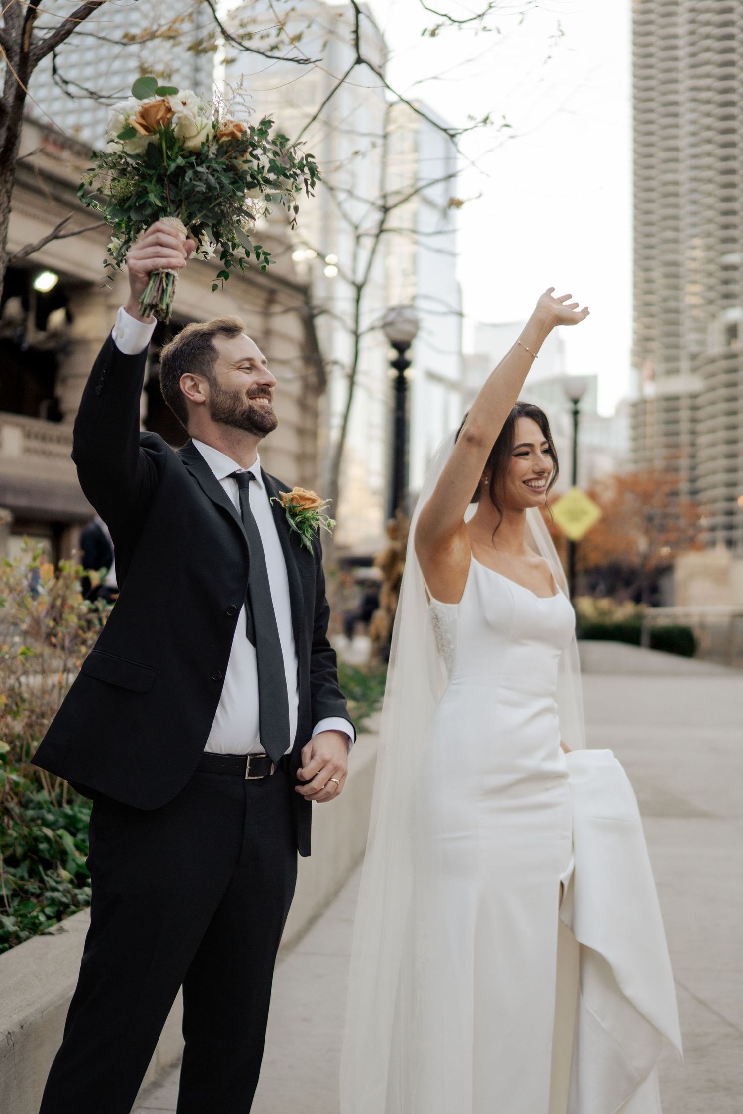 Celebrating newlyweds raising arms with bouquet on Chicago Riverwalk after their wedding ceremony.