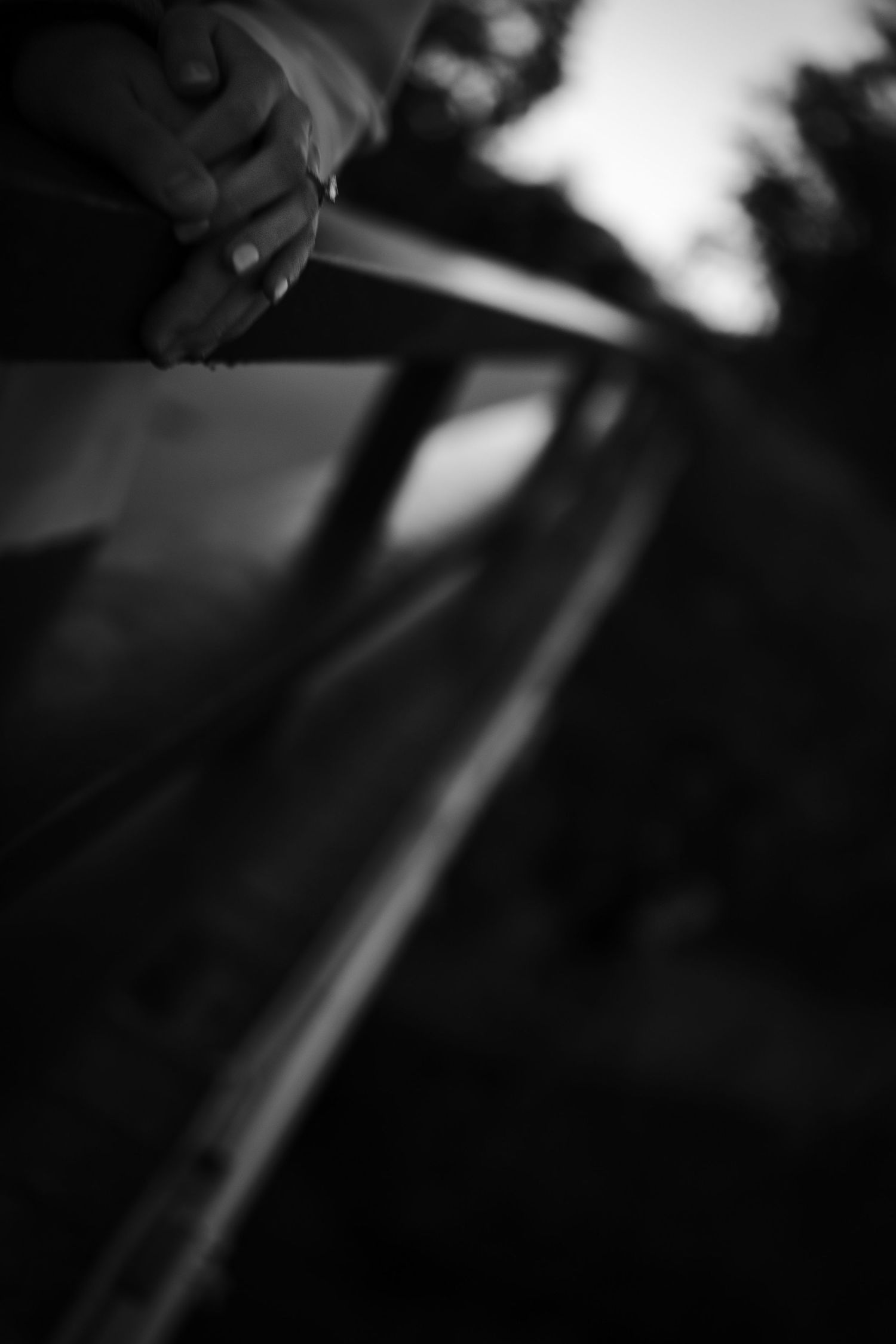 Black and white close-up of an engaged couple holding hands on a railing at dusk.