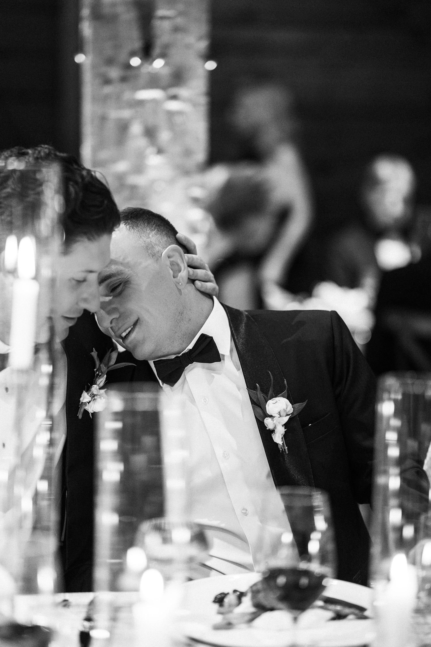 Black and white photo of groom laughing at wedding reception table.