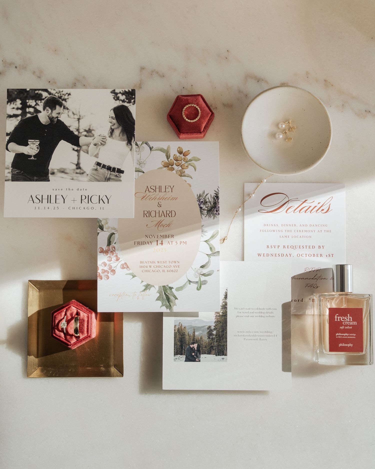 Elegant wedding invitation suite with floral details, ring boxes, and perfume on marble surface.