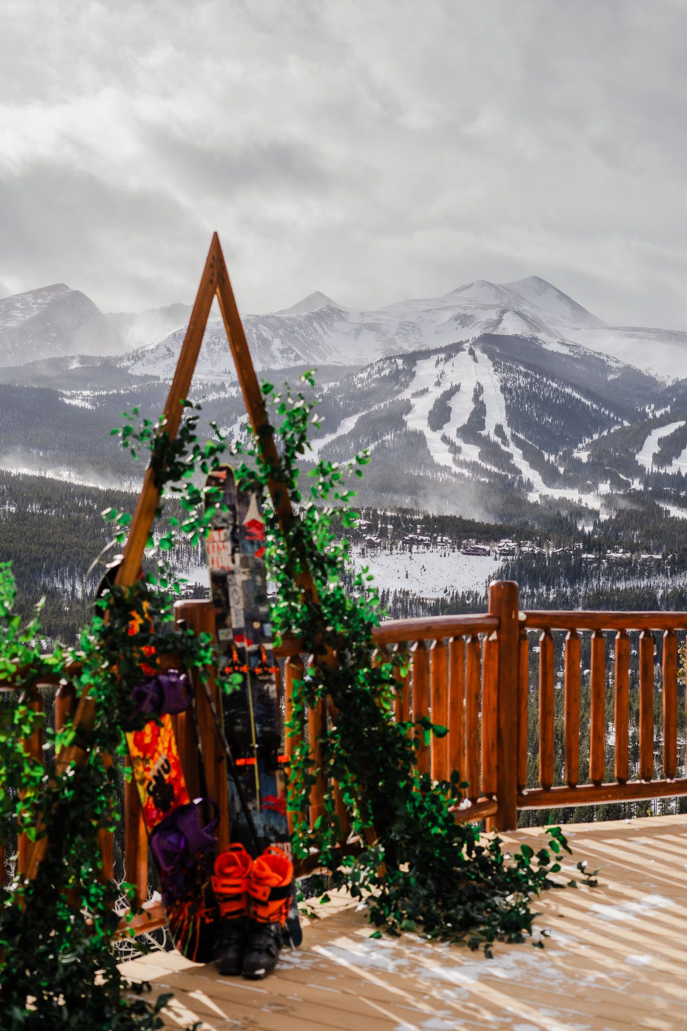 A wooden arch decorated with green ivy and colorful flowers on a snowy mountain wedding deck in Breckenridge.