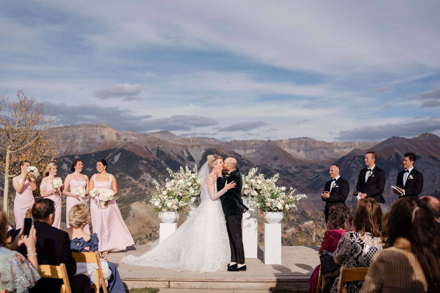 Outdoor mountain wedding ceremony with bride and groom at altar, bridesmaids in pink, groomsmen in black.