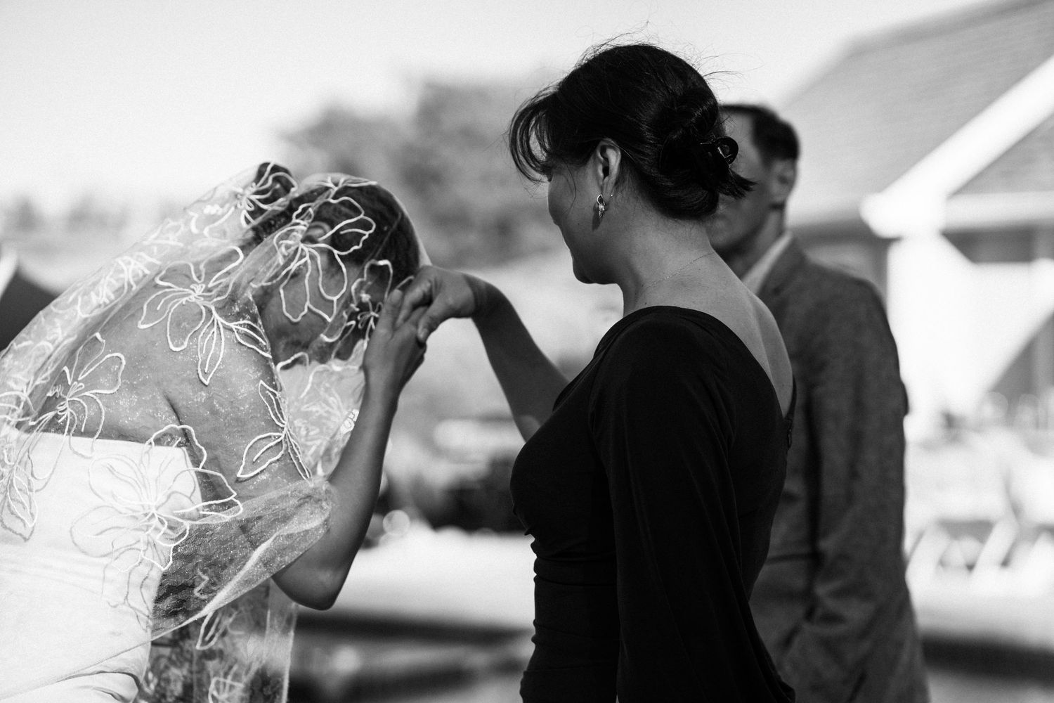 Black and white photo of emotional bride in lace veil being comforted by woman outdoors before ceremony.