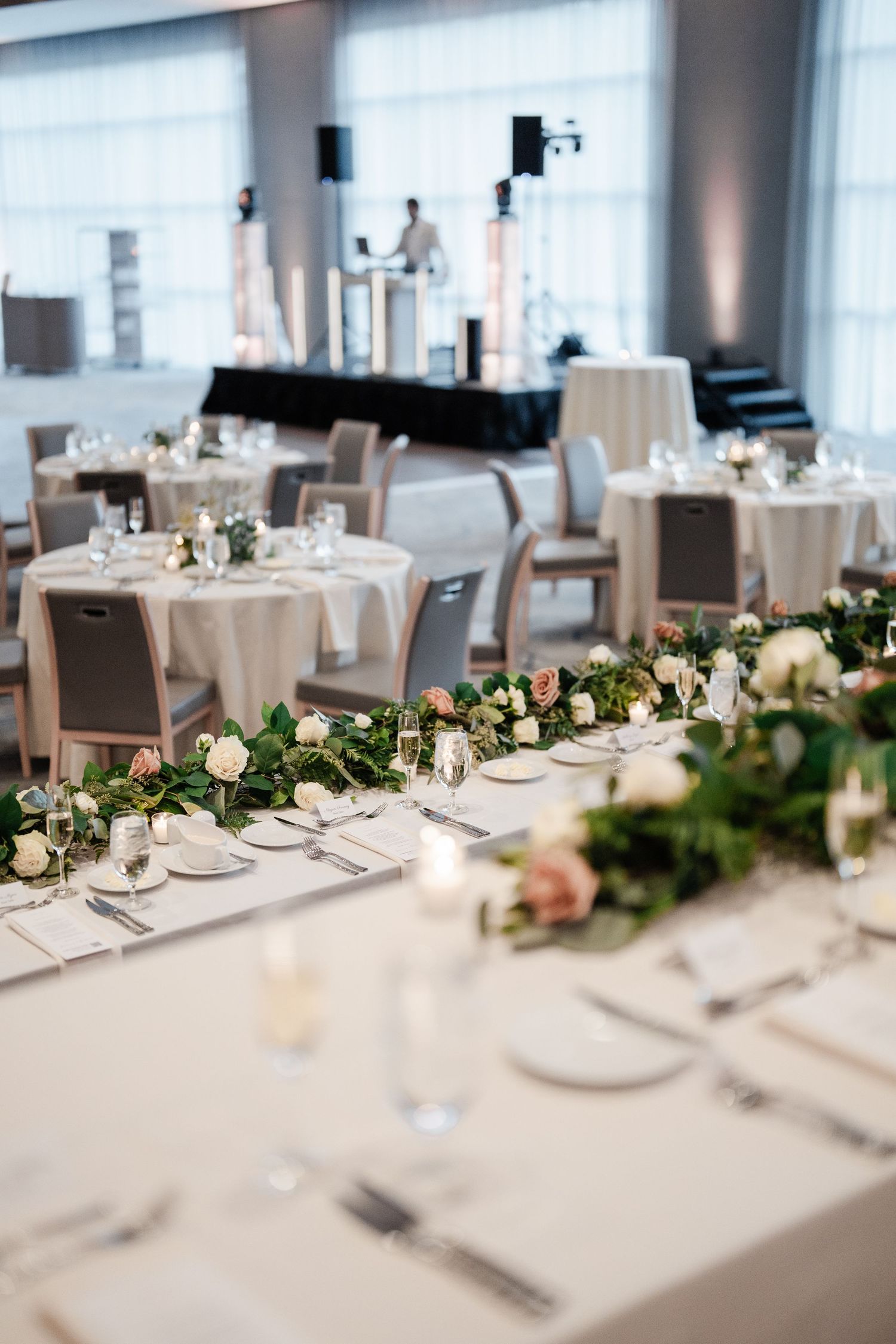 Elegant wedding reception with floral garland centerpiece on head table and round guest tables in modern ballroom.