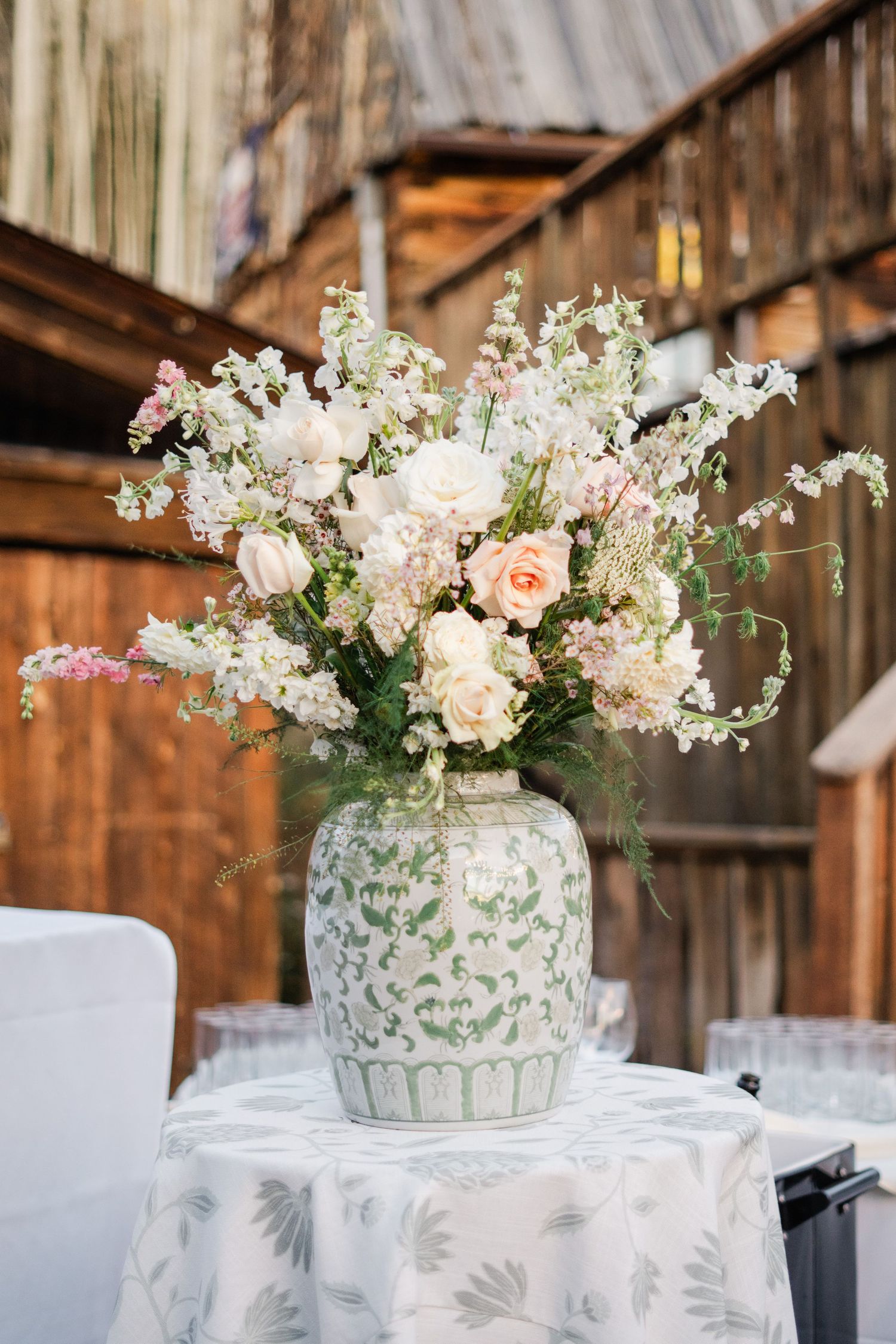 Large white and pink floral arrangement in green ceramic vase on table at rustic barn wedding.