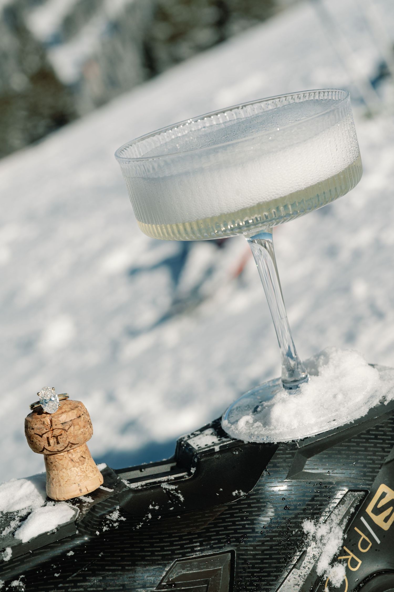 Elegant champagne coupe filled with Prosecco resting on snow-covered ski boot outdoors.