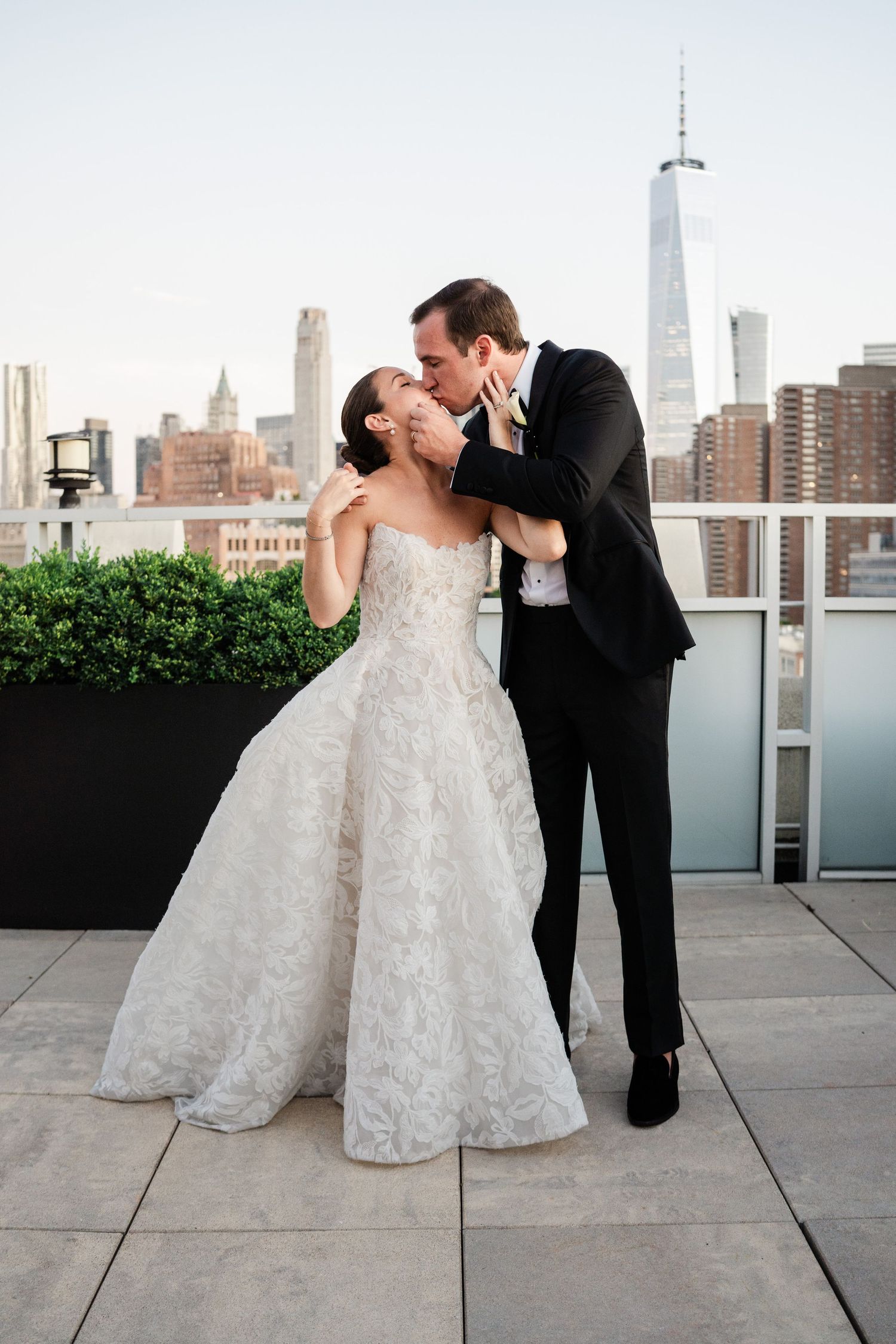 Bride and groom share a kiss on a rooftop terrace with the New York City skyline and One World Trade Center.
