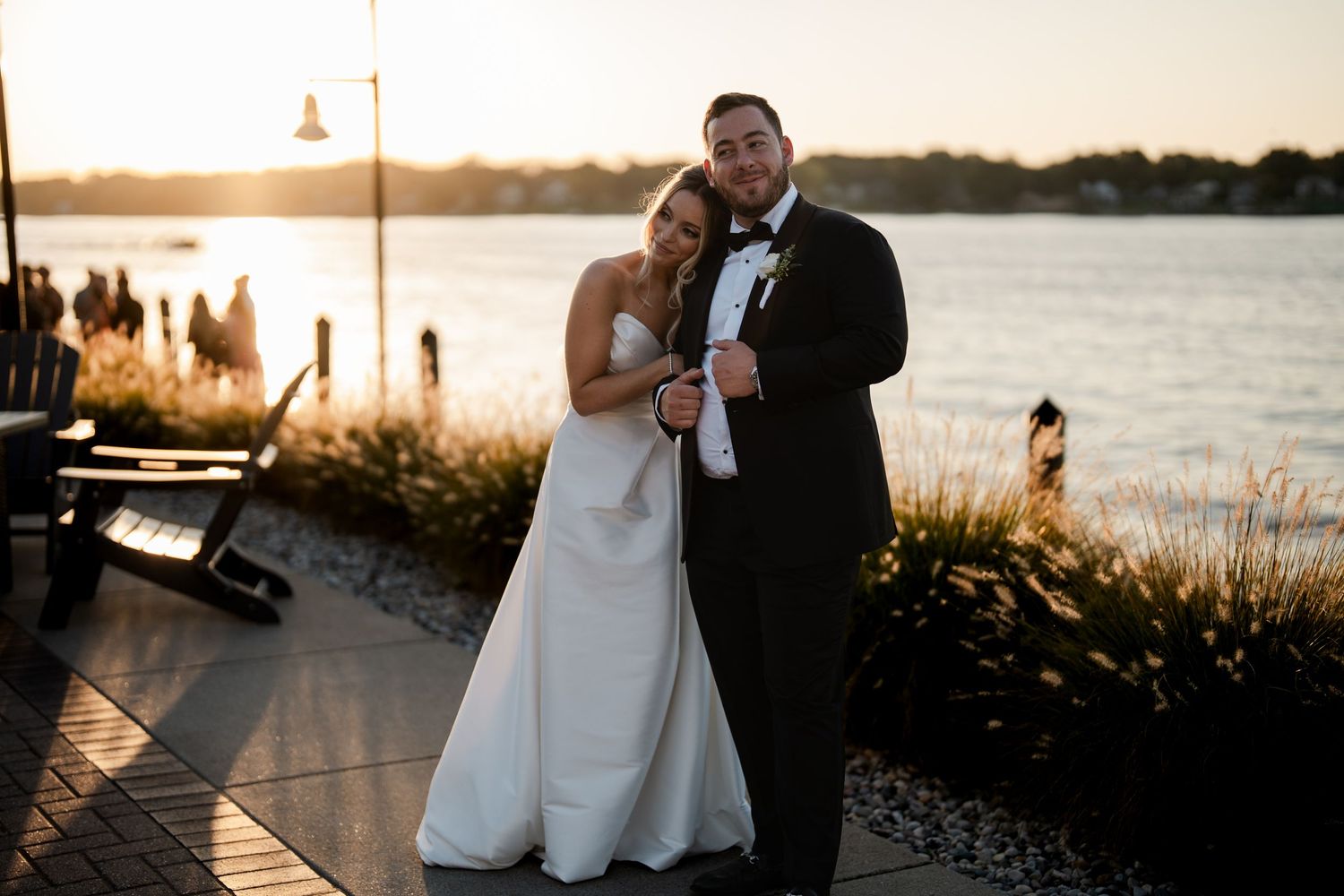 Bride and groom pose together at waterfront sunset wedding venue.
