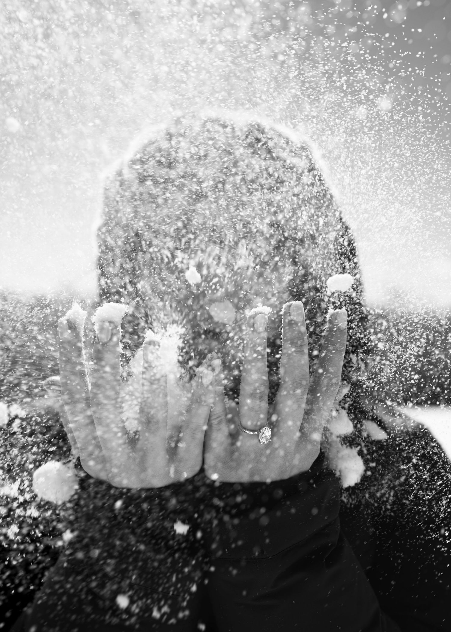 Person shielding face with hands as snow explodes around them in black and white.