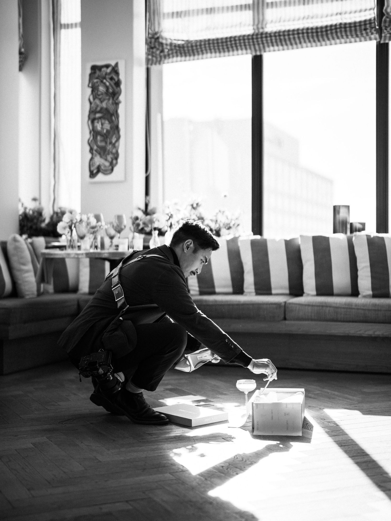 Wedding photographer crouches to capture detail shot in sunlit modern interior space.