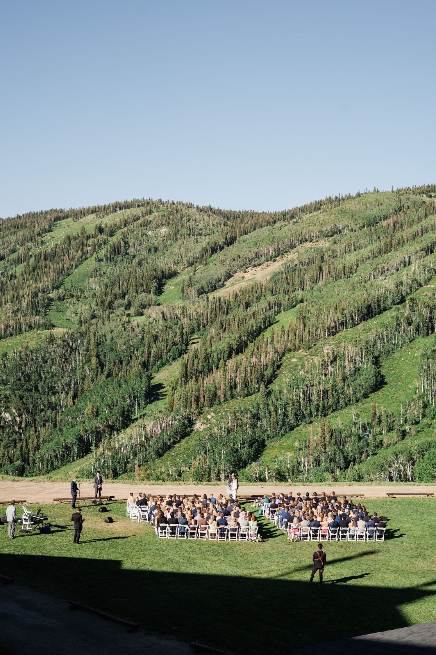 Aerial view of outdoor wedding ceremony set against lush green mountain slopes.