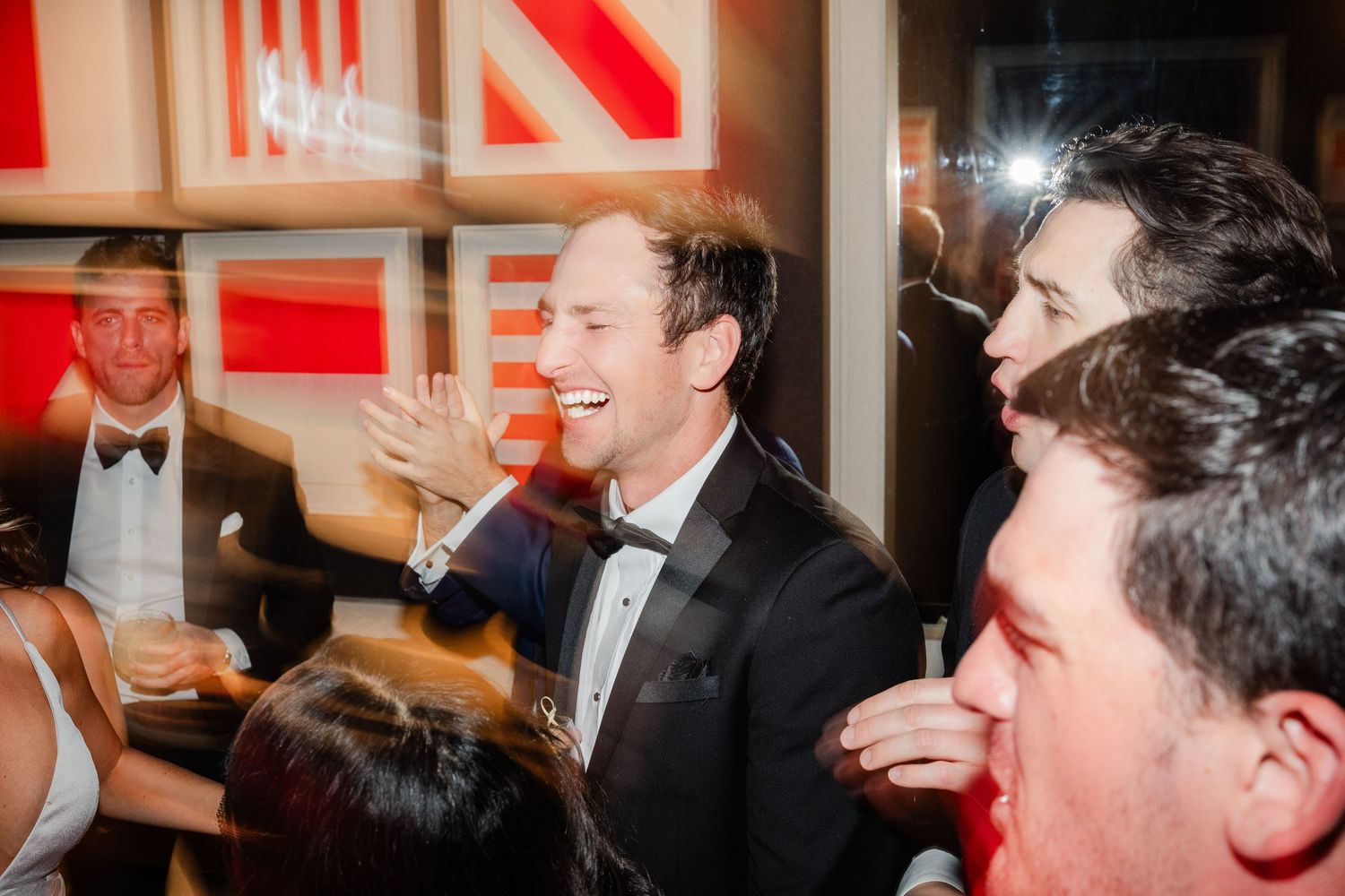 Groom in tuxedo laughs and dances with guests at a lively wedding reception party.