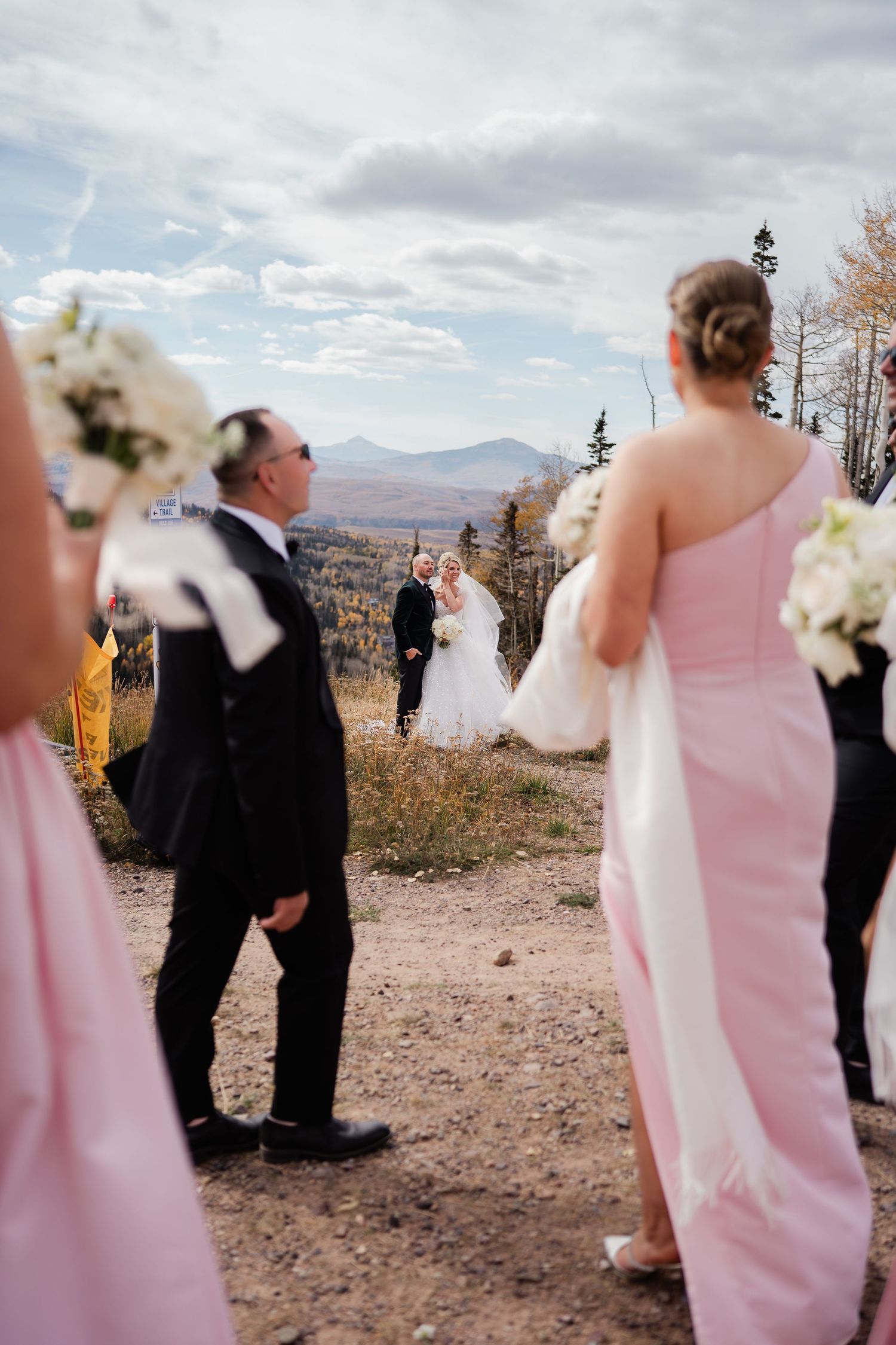 Bride and groom sharing first look moment on mountain hilltop while wedding party watches in background.