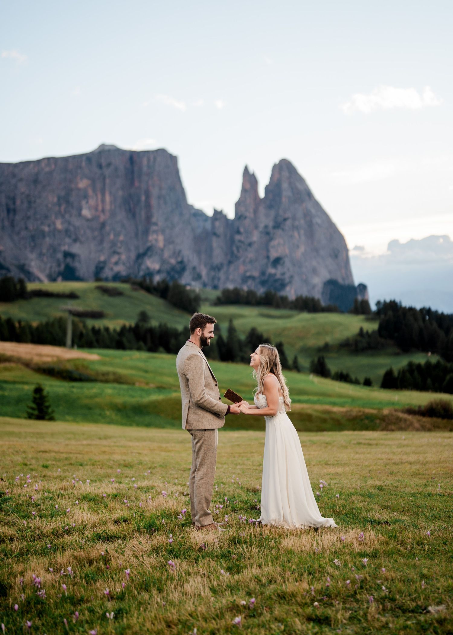 Bride and groom exchange vows in a lush green meadow with dramatic Dolomite mountains behind them.