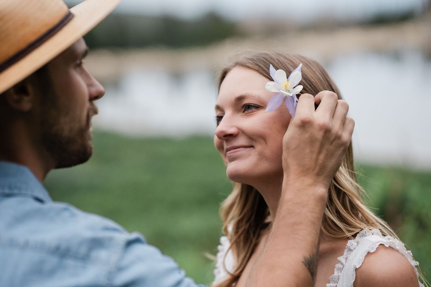 Man in tan hat gently placing a small flower in smiling womans hair during outdoor engagement session.