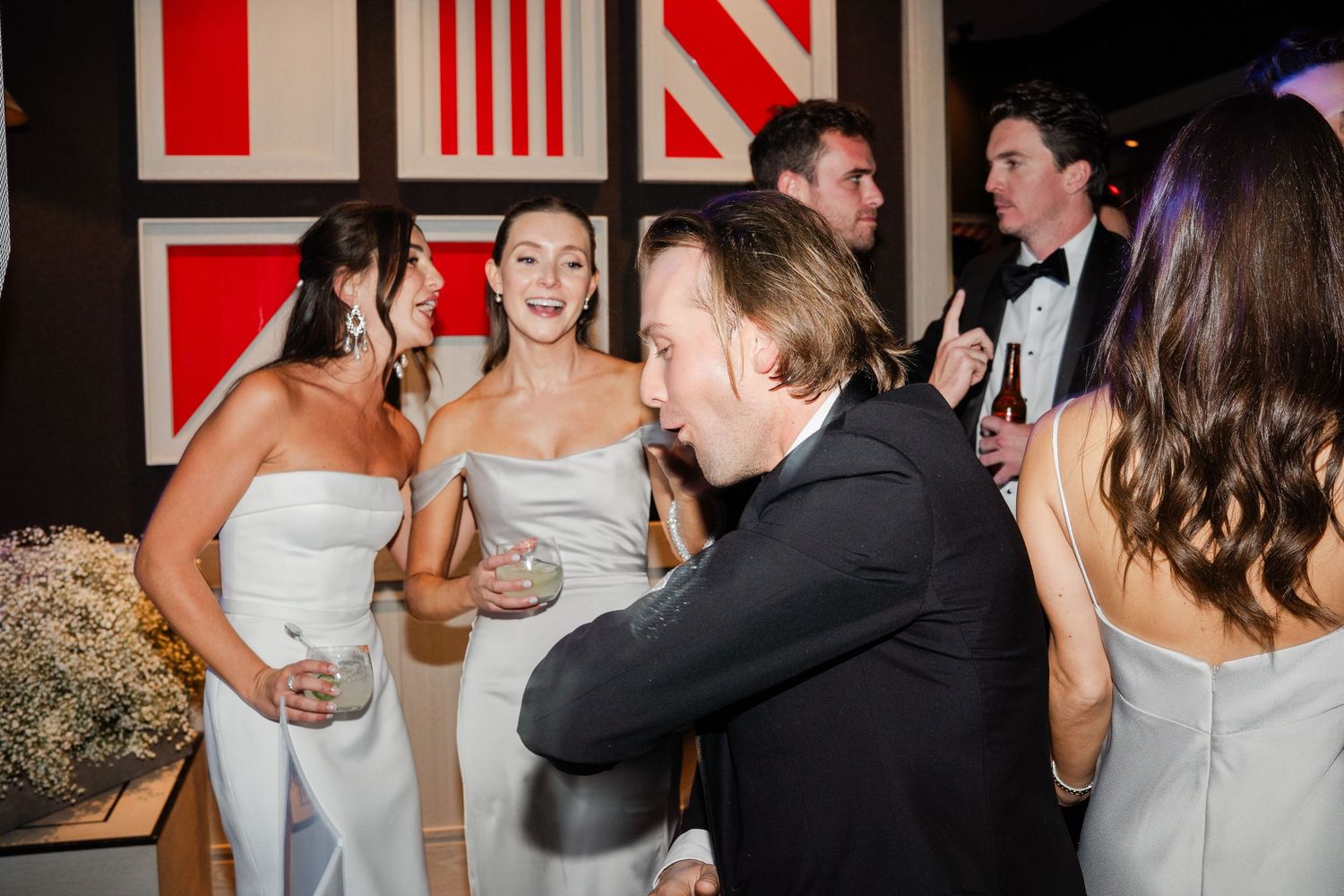 Bridesmaids in white dresses and guests mingling joyfully at a stylish wedding reception.