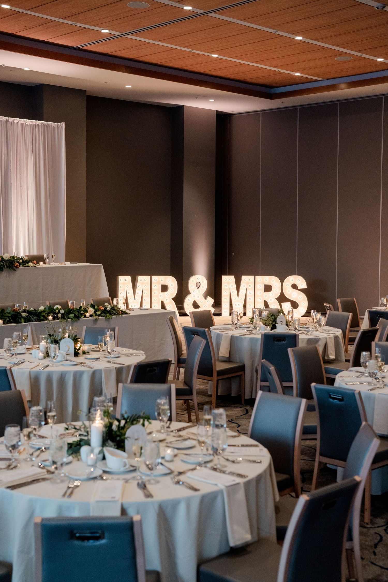 Wedding reception ballroom with illuminated MR & MRS marquee letters and elegantly set round tables.