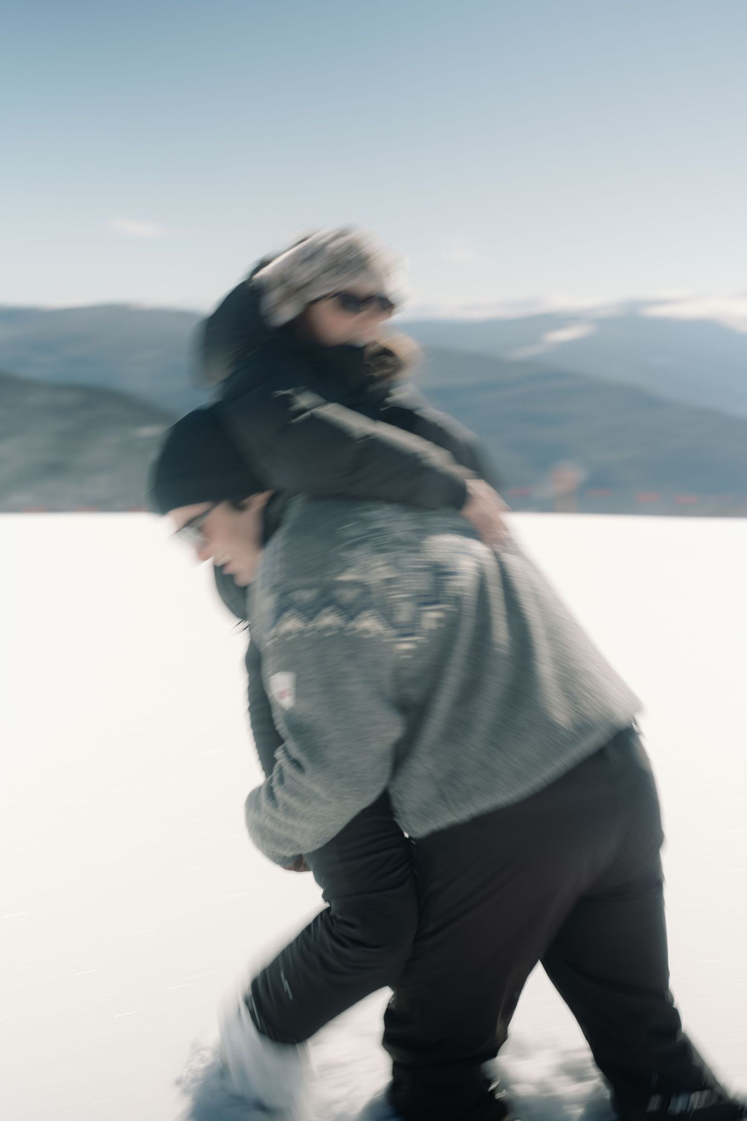 Motion blur artistic photo of couple doing piggyback ride on snowy mountain slope.