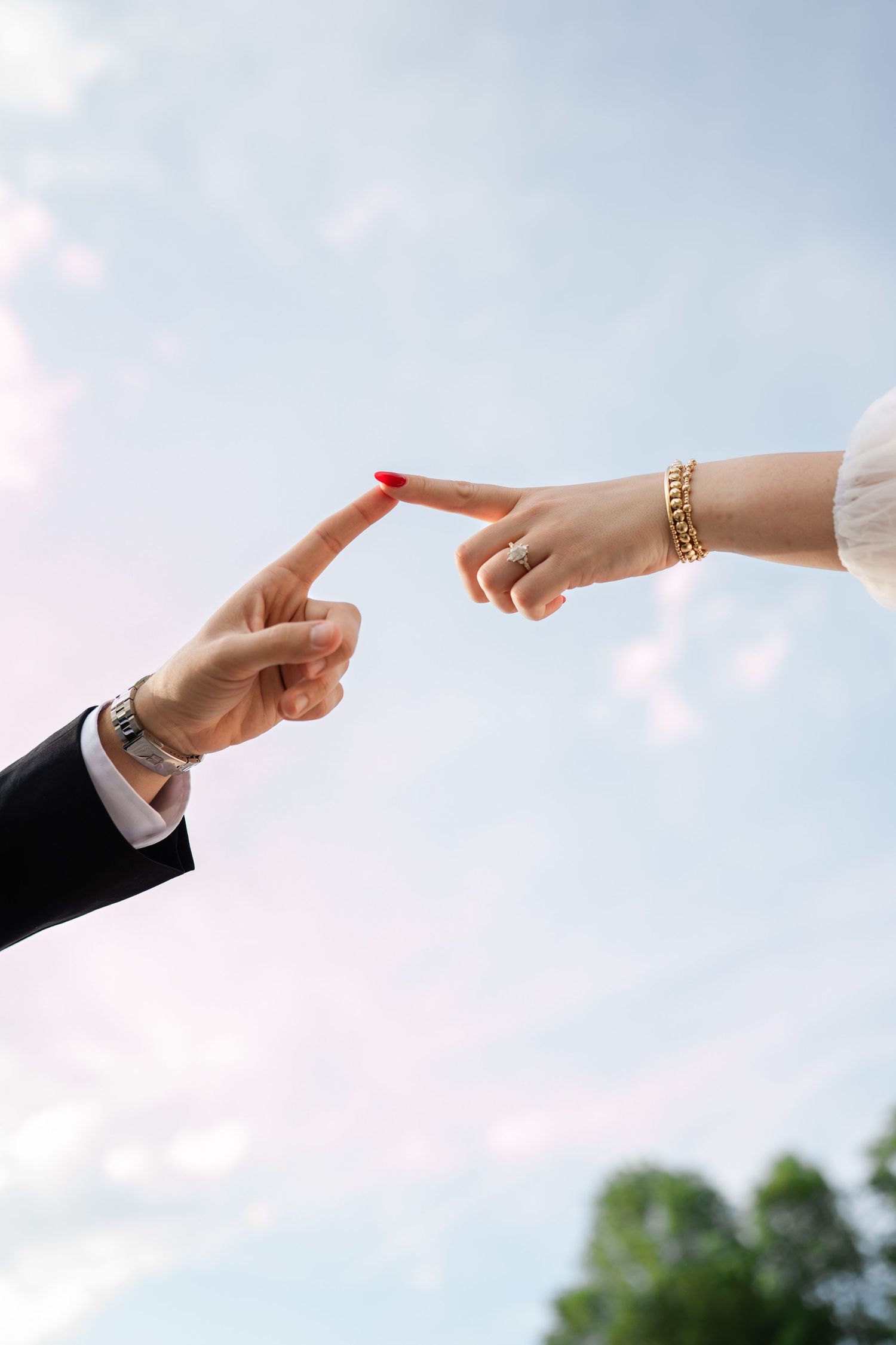 Close-up of bride and groom touching fingertips against a blue sky in a romantic gesture.