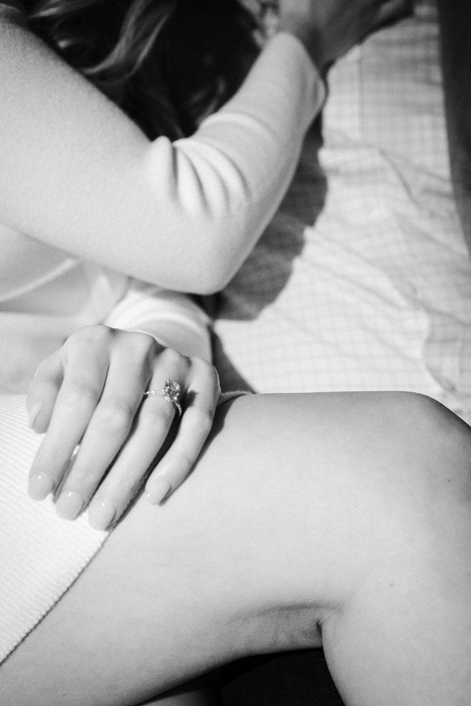 Black and white close-up of woman's hand adorned with elegant diamond engagement ring resting on knee.