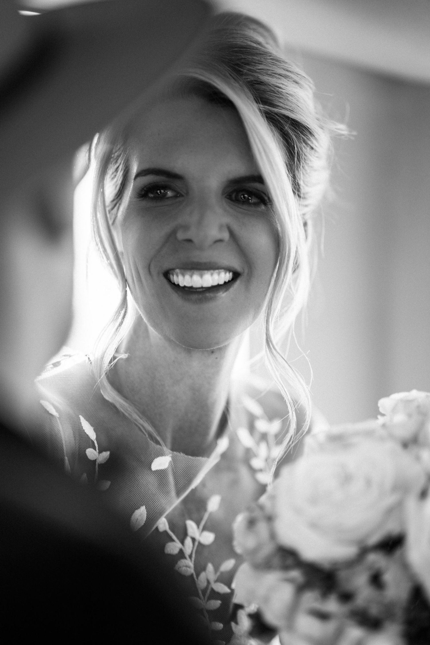 Black and white portrait of a smiling blonde bride holding a bouquet at her wedding.
