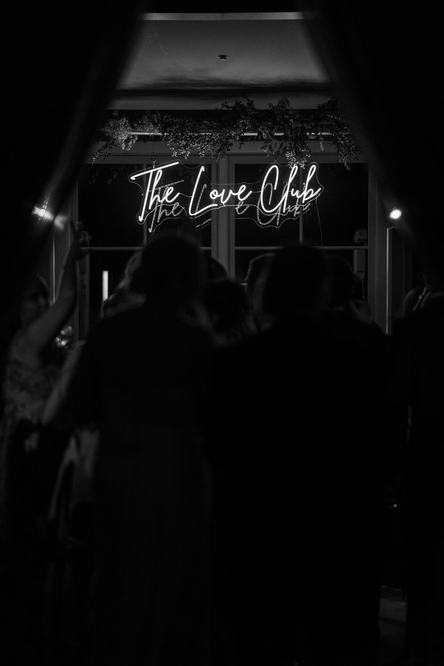 Black and white photo of guests entering a venue under a glowing neon sign reading The Love Club.
