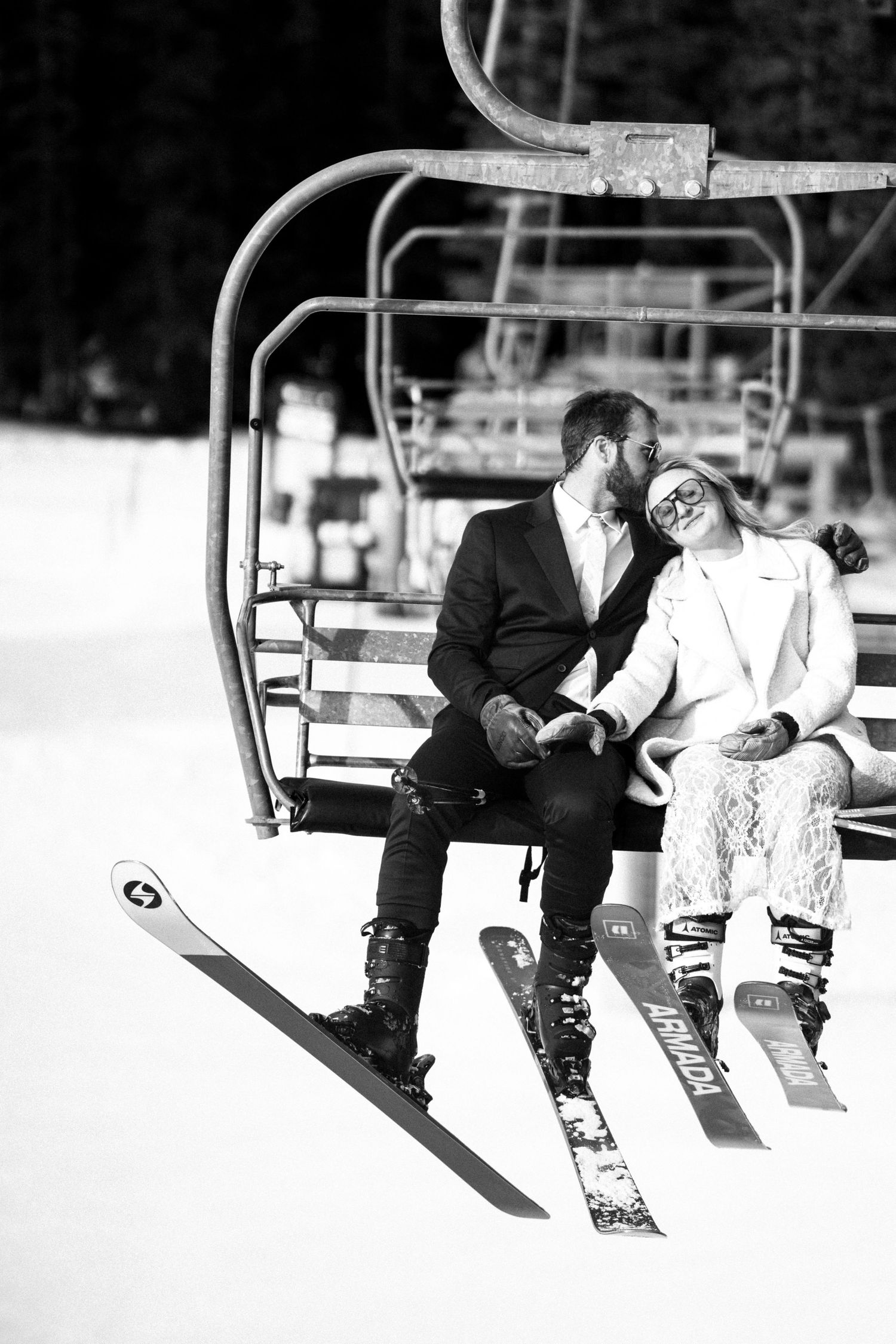 Bride and groom riding ski lift together in wedding attire, black and white winter elopement photo.