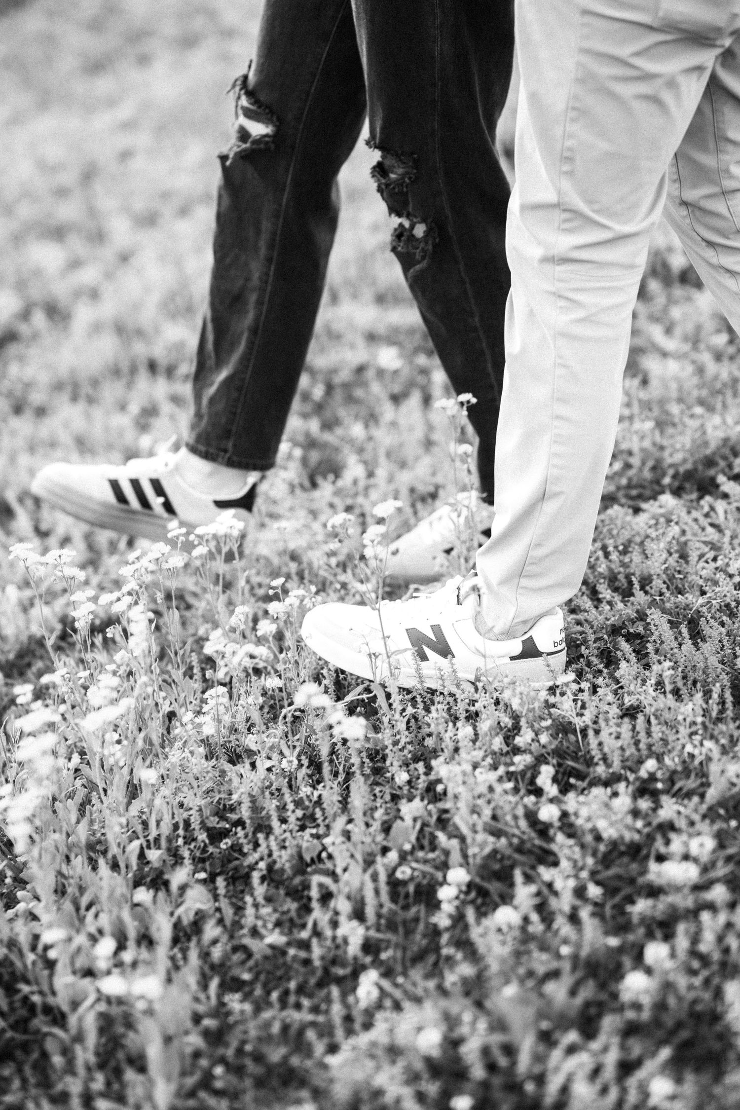 Black and white close-up of couples feet in sneakers standing in a wildflower meadow.