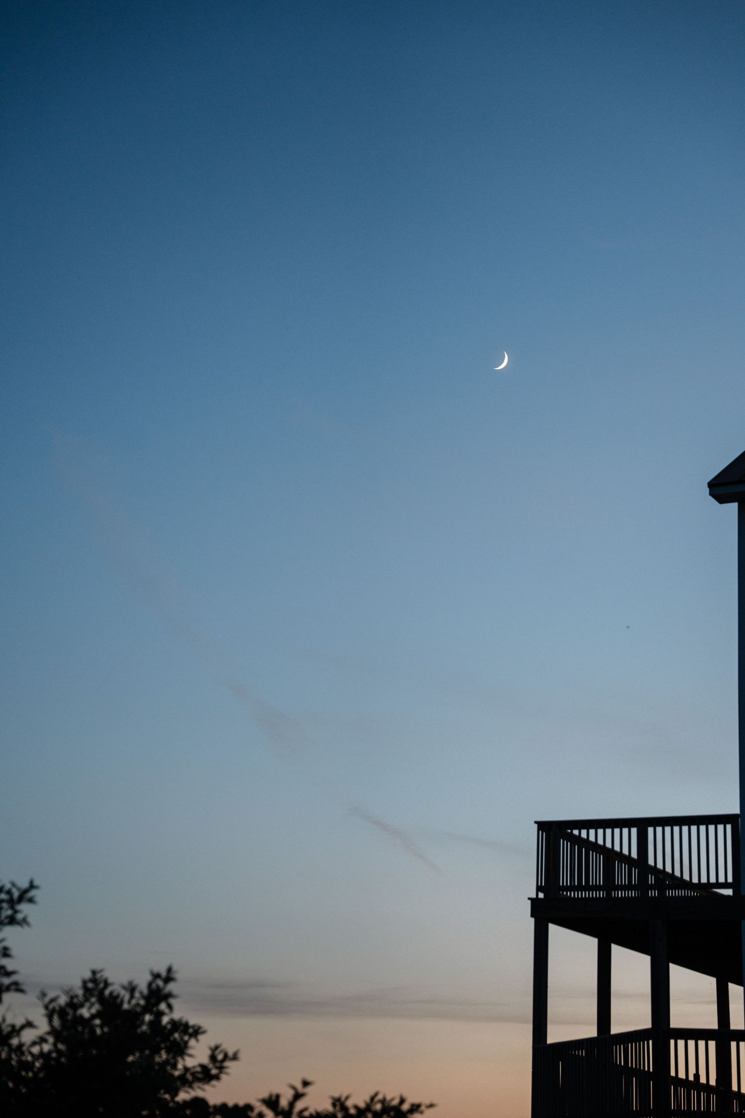 A crescent moon rises in a twilight blue sky above a wooden deck silhouette.