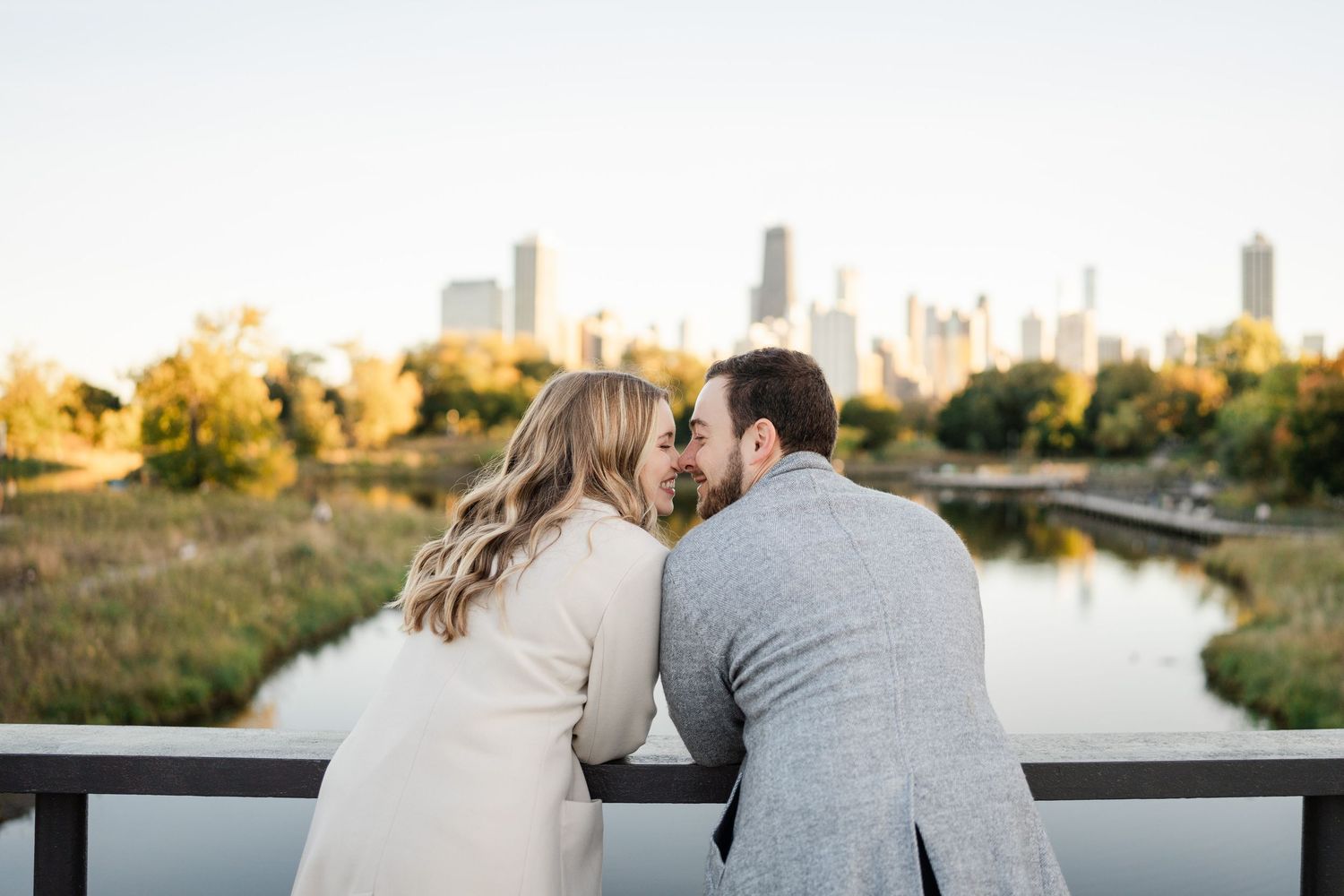 Couple sharing an intimate moment on a bridge overlooking a river with Chicago skyline at sunset.
