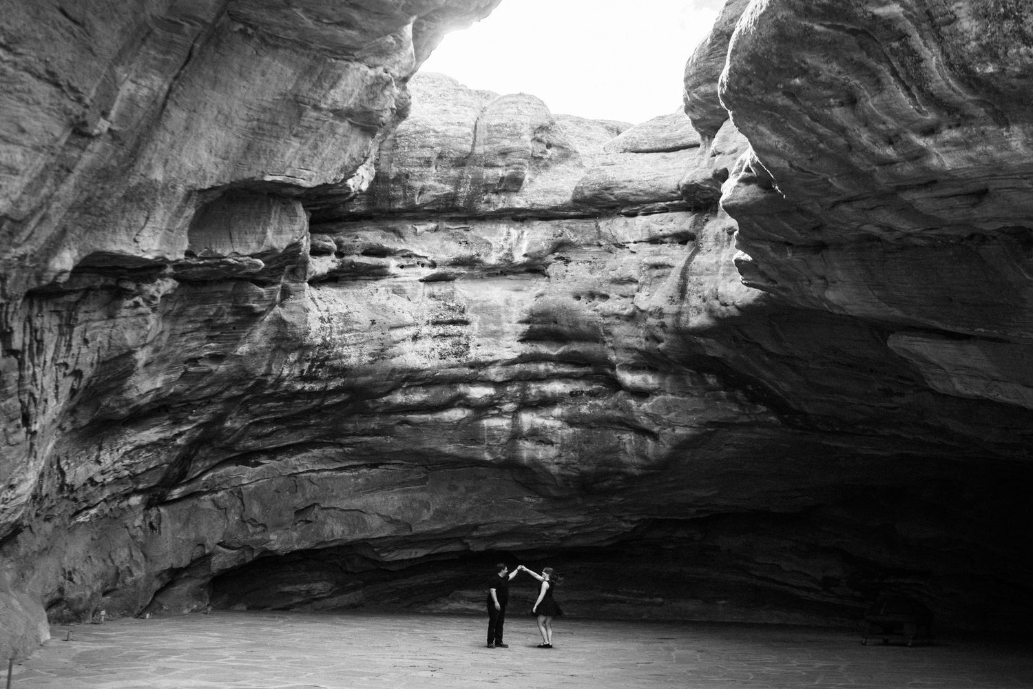 Black and white photo of a lone person standing inside a dramatic sandstone cave arch.