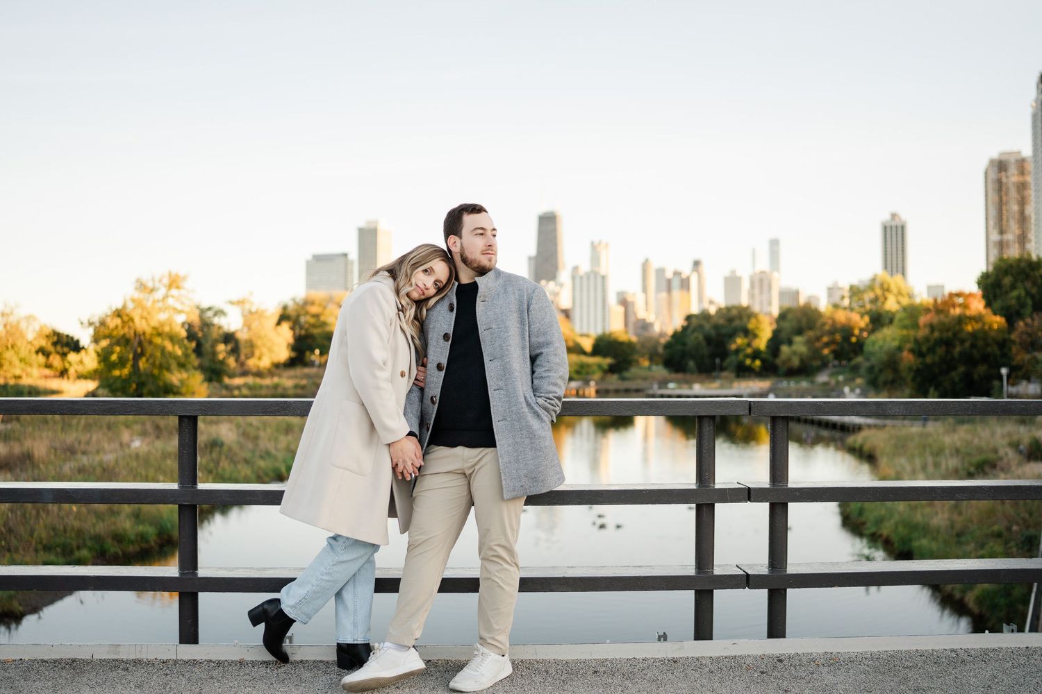 Stylish engaged couple standing together on a bridge with the Chicago skyline at golden hour.