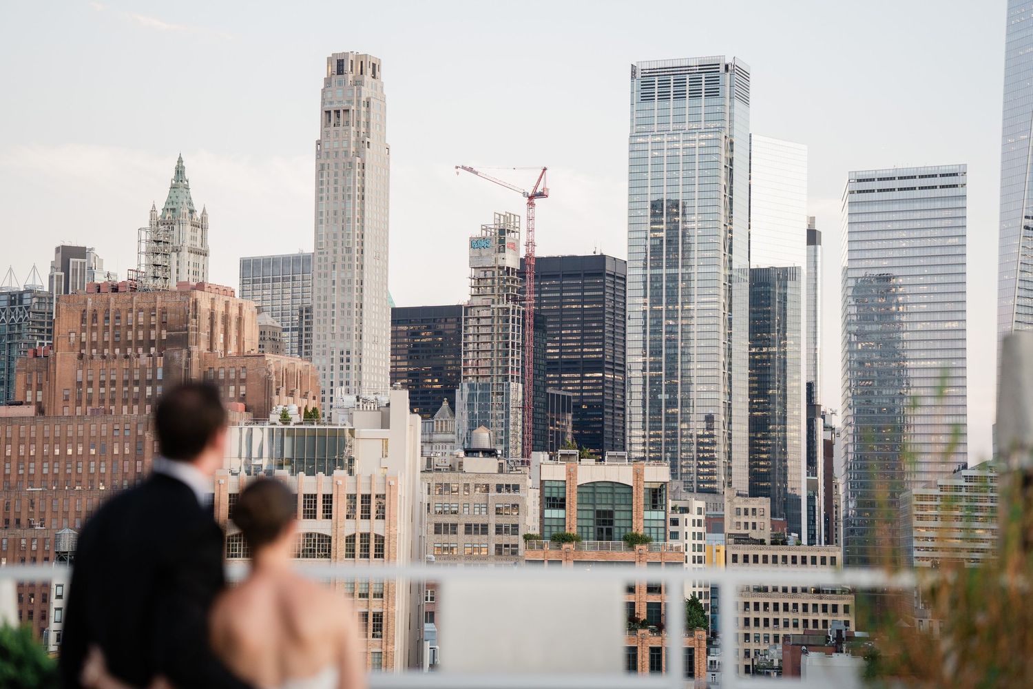 Bride and groom admiring stunning New York City skyline from rooftop terrace on their wedding day.