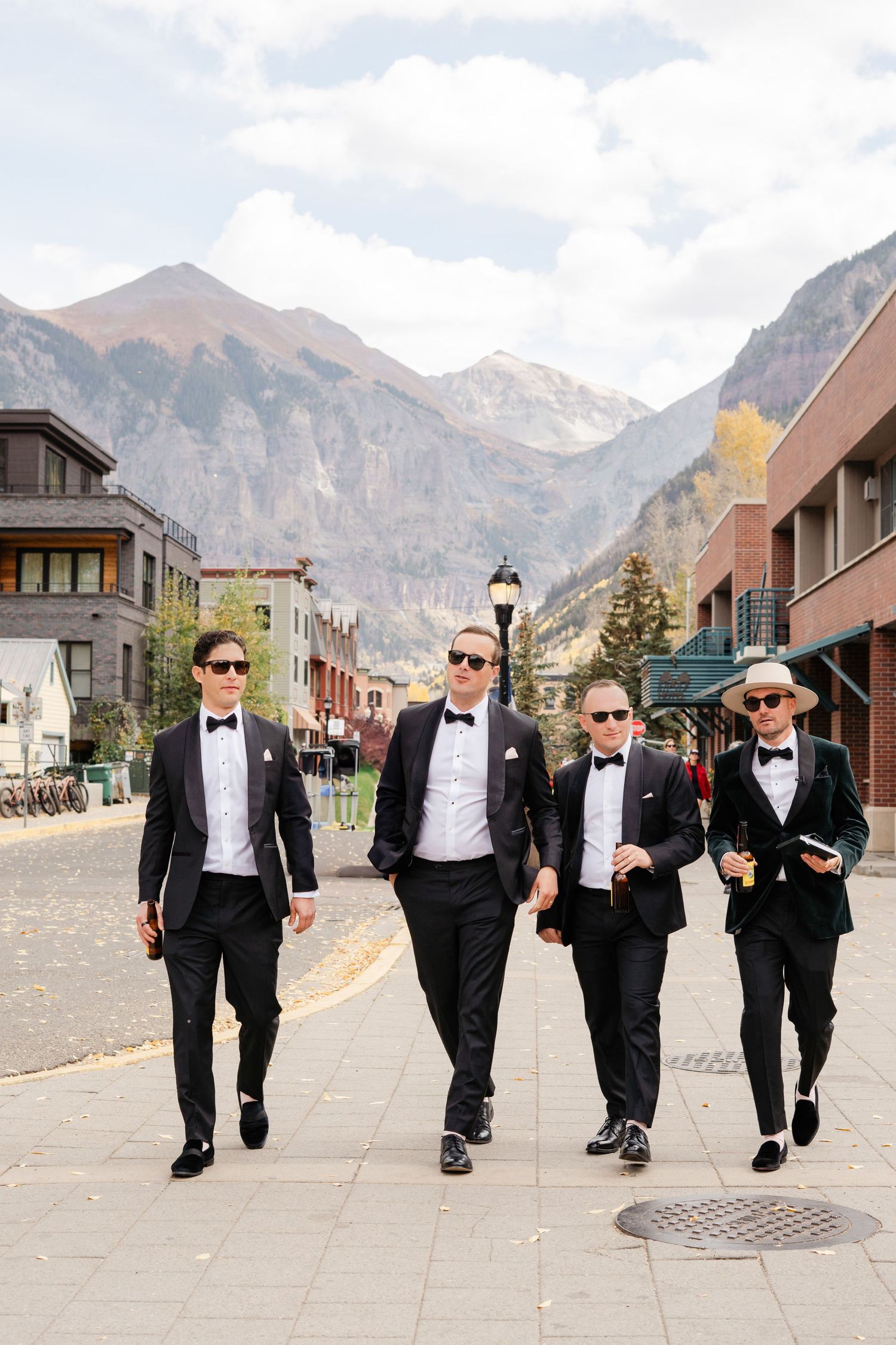 Four groomsmen in black tuxedos walking down a cobblestone street with mountain backdrop in Telluride Colorado.
