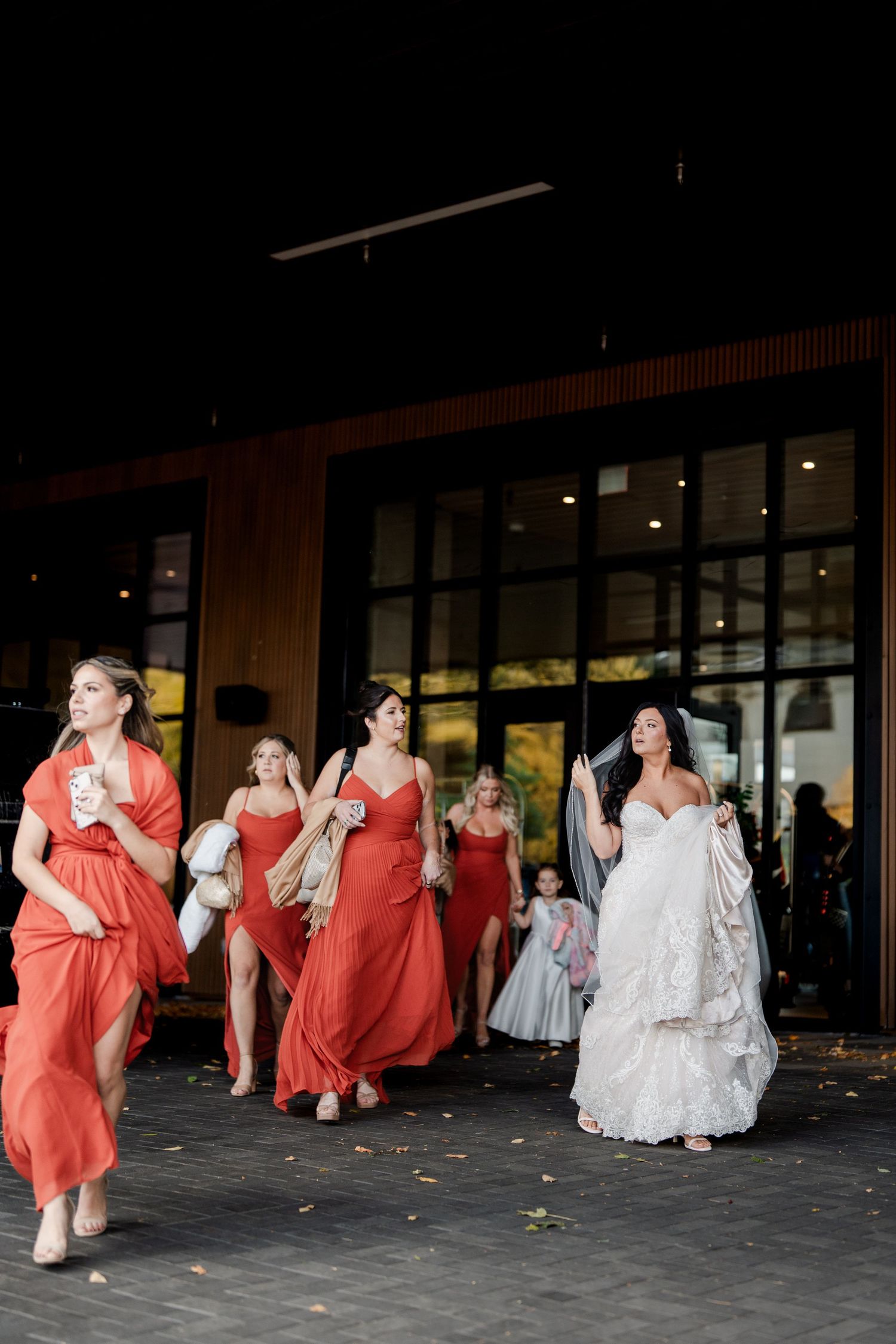Bride in white gown and bridesmaids in red dresses walking outside at night during wedding celebration.