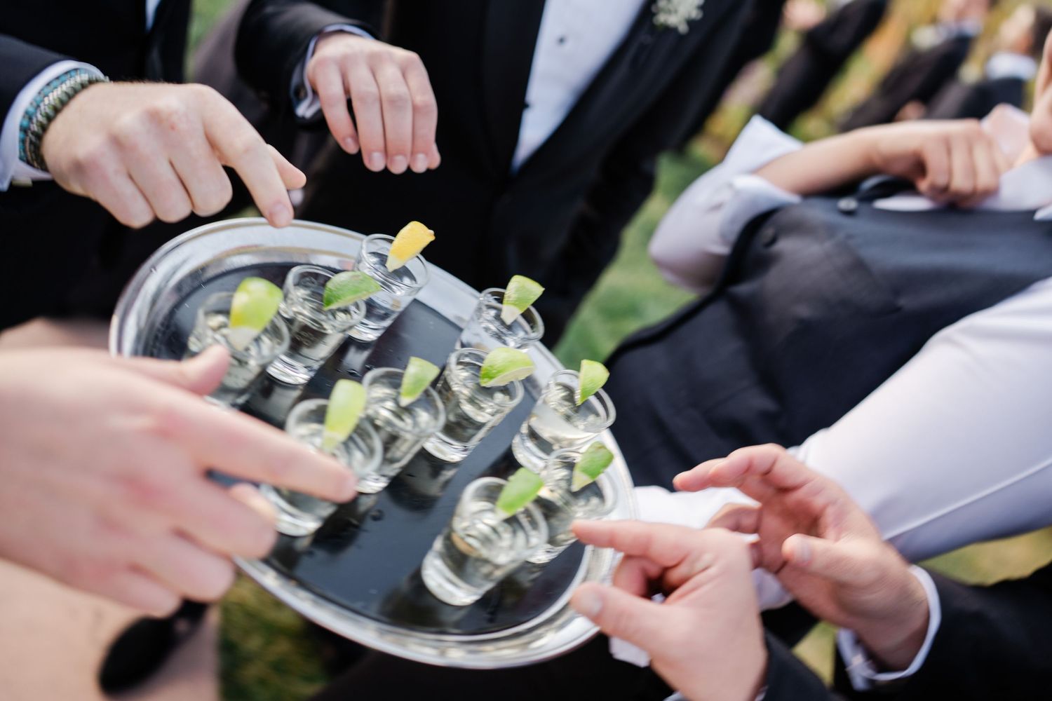 Wedding guests reaching for shot glasses with lime garnishes on a silver tray at a reception.