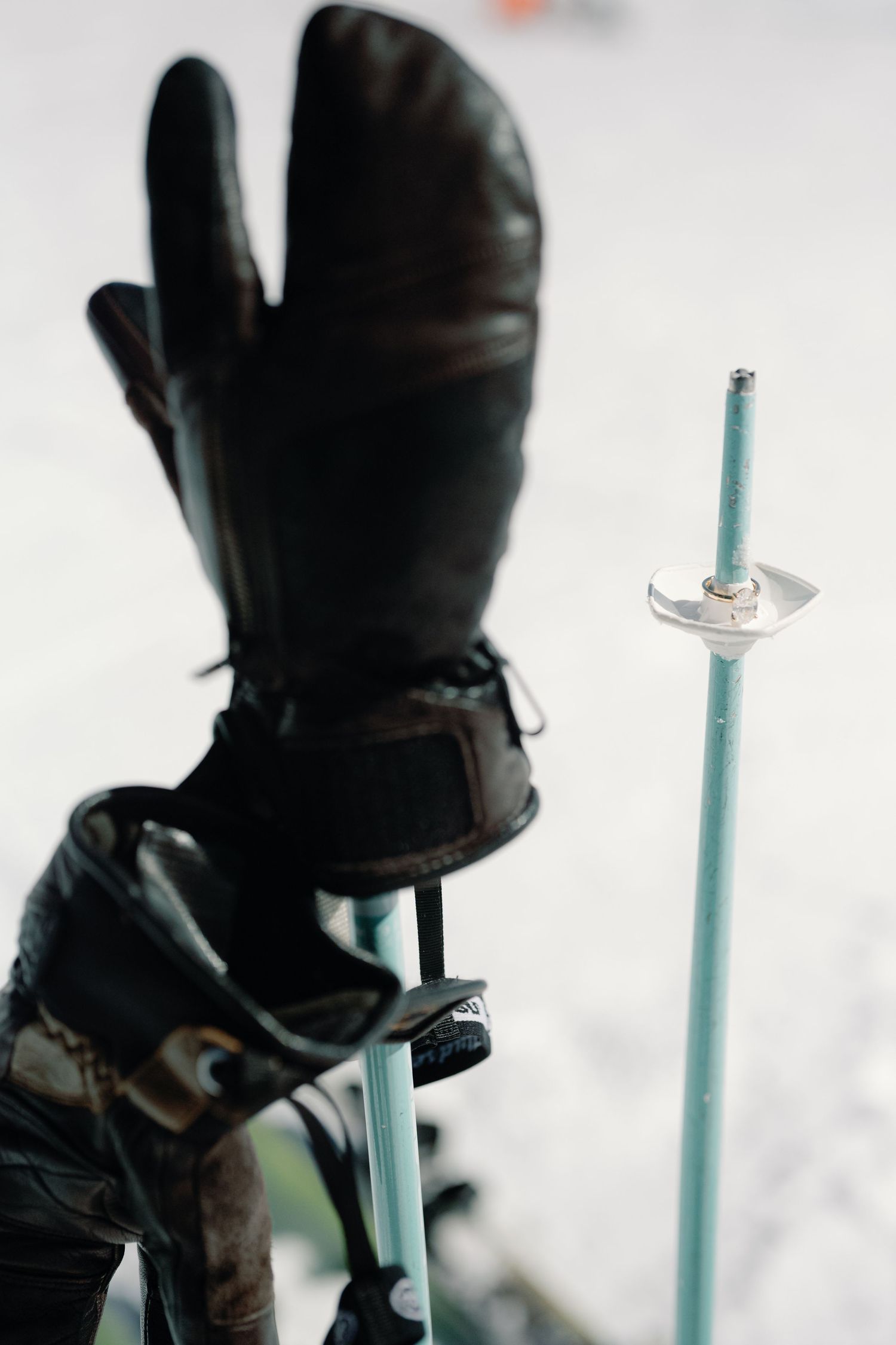 Close-up of a leather ski mitten gripping a ski pole against a snowy white background during a winter ski day.