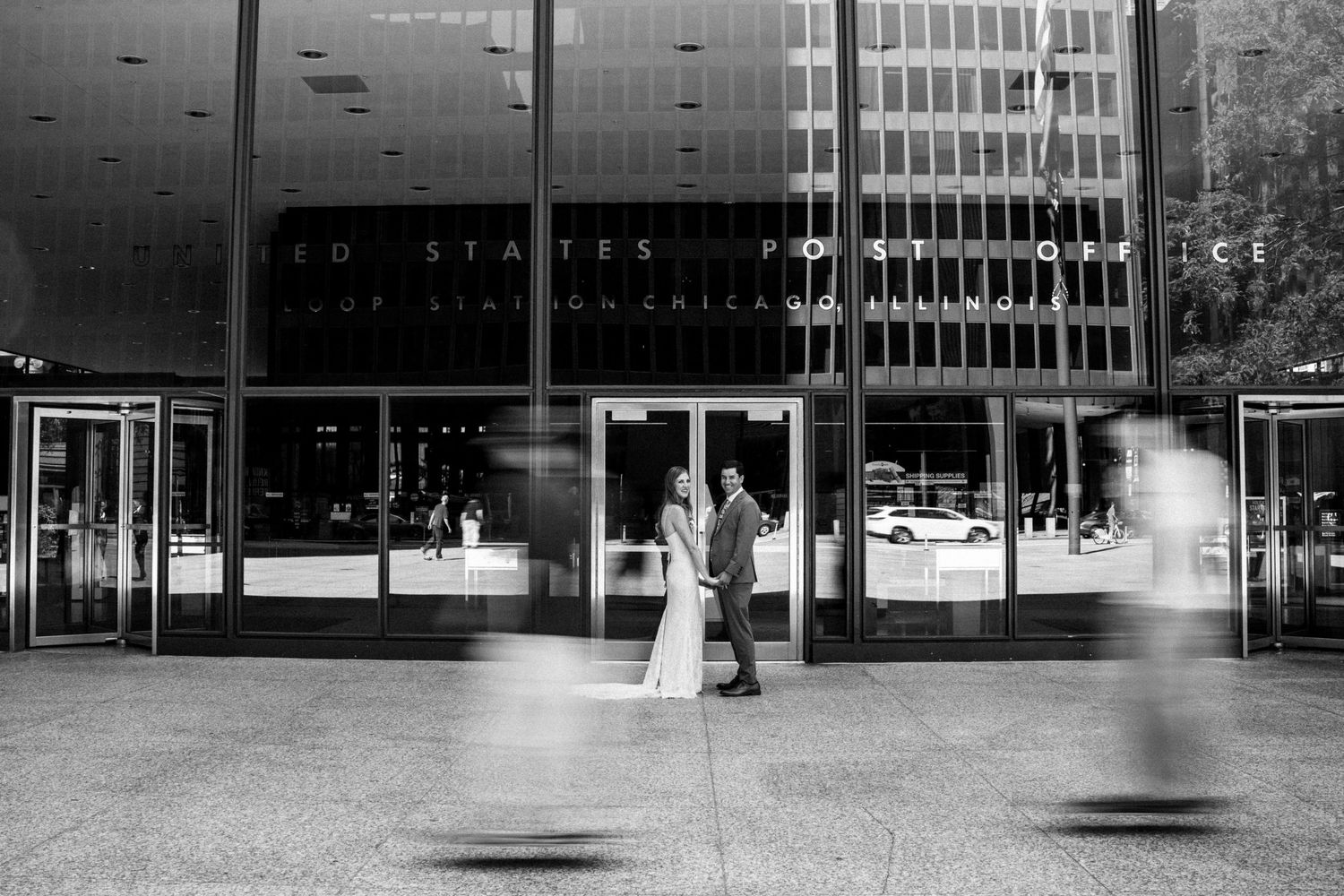 Bride and groom share intimate moment outside US courthouse entrance with blurred pedestrians passing by.