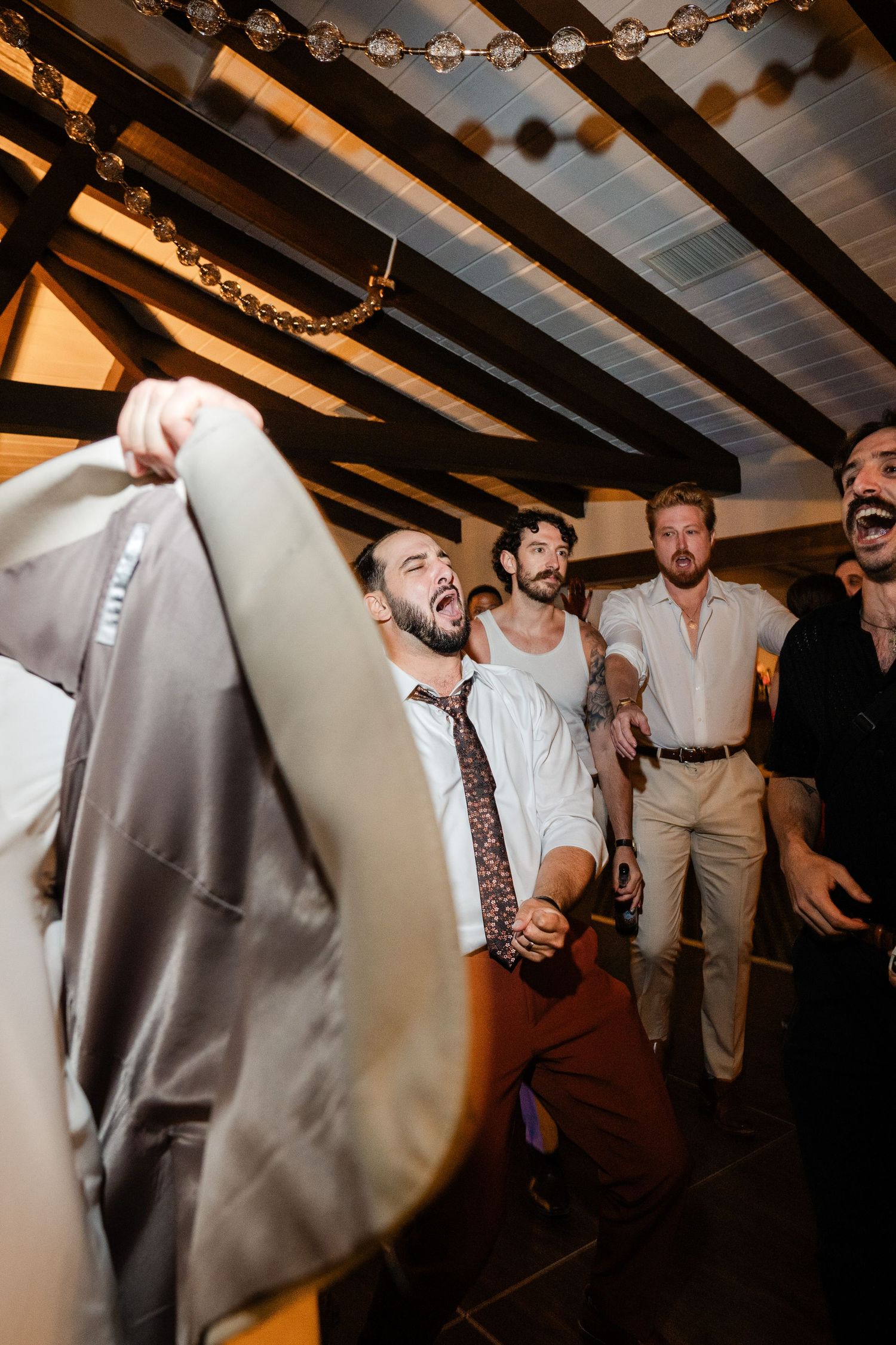 Energetic wedding guest dancing and waving jacket in the air at a fun indoor reception party.
