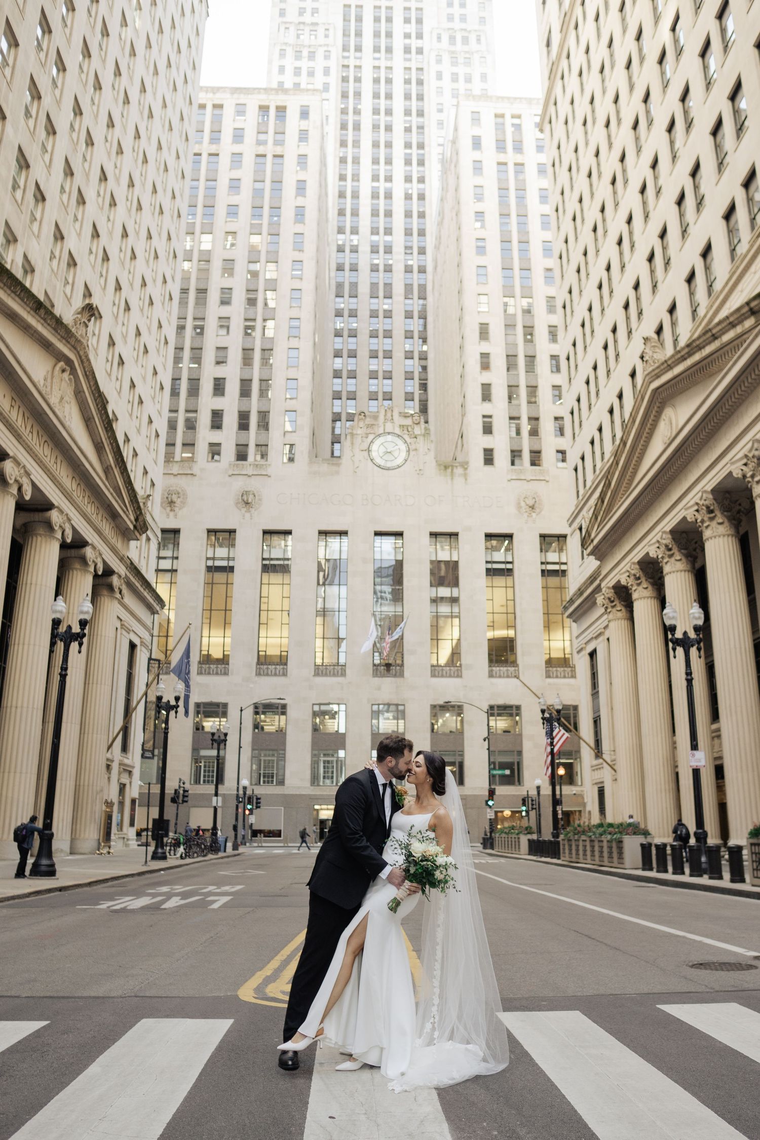 Bride and groom kissing on crosswalk in front of Chicago Board of Trade building.