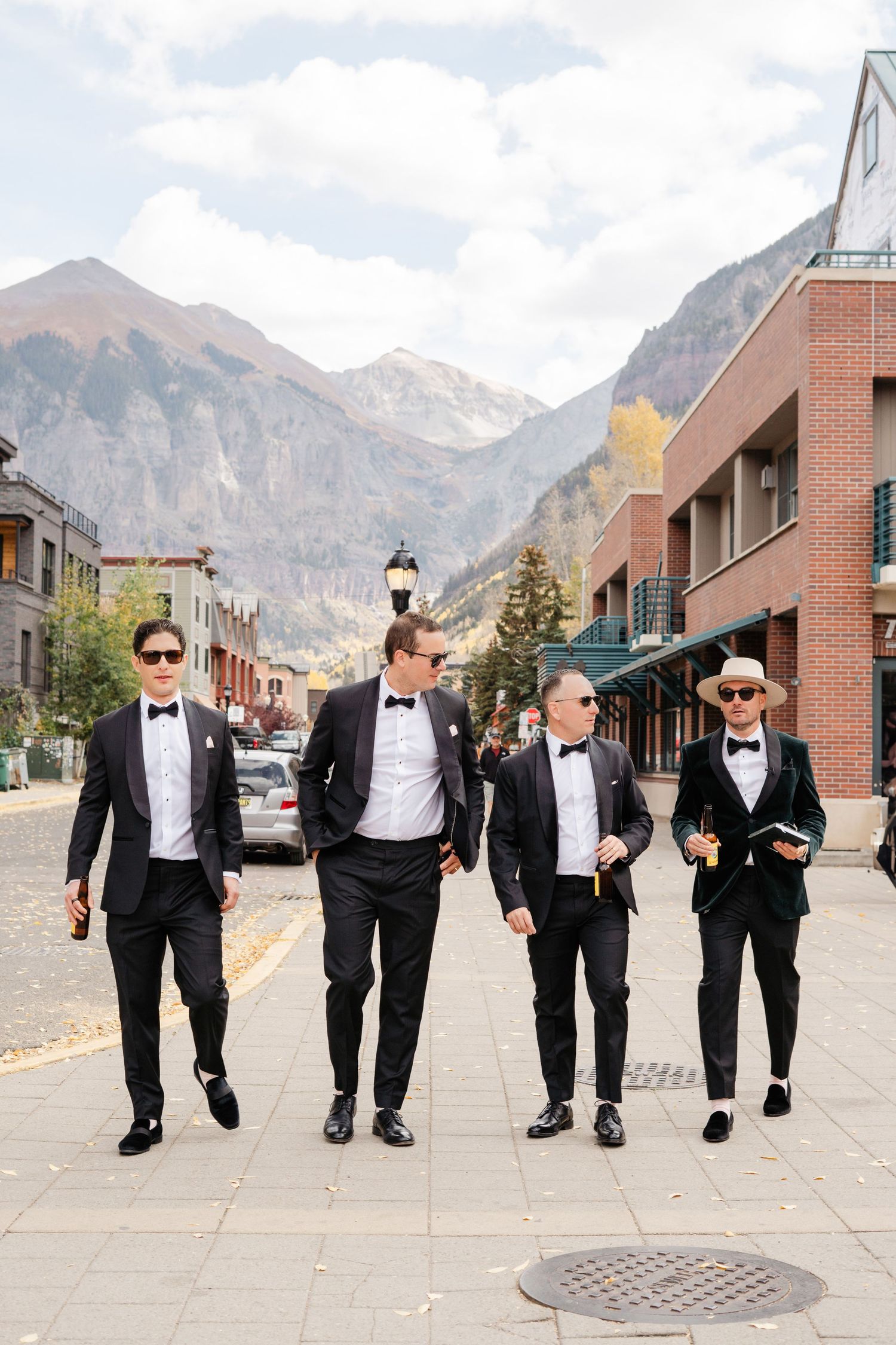 Four groomsmen in black tuxedos walking together on a street with mountain views in Telluride.
