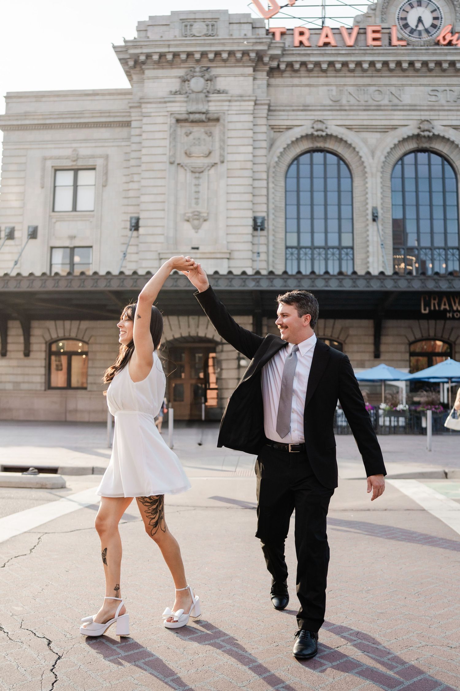 Couple dancing outside Denver Union Station, bride in white mini dress and groom in black suit.