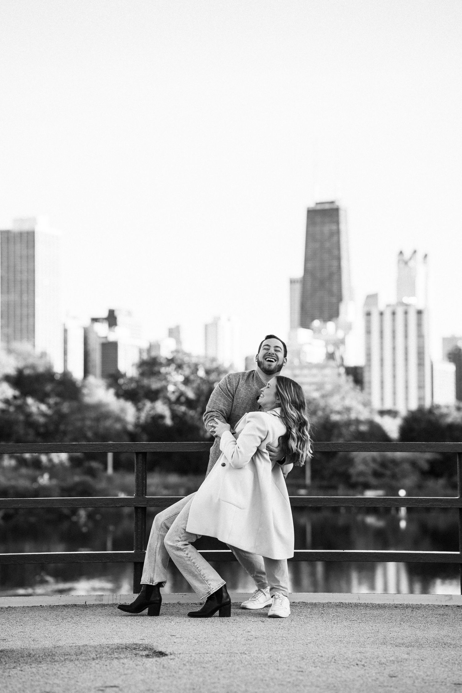Black and white photo of a joyful couple playfully posing with the Chicago skyline behind them.