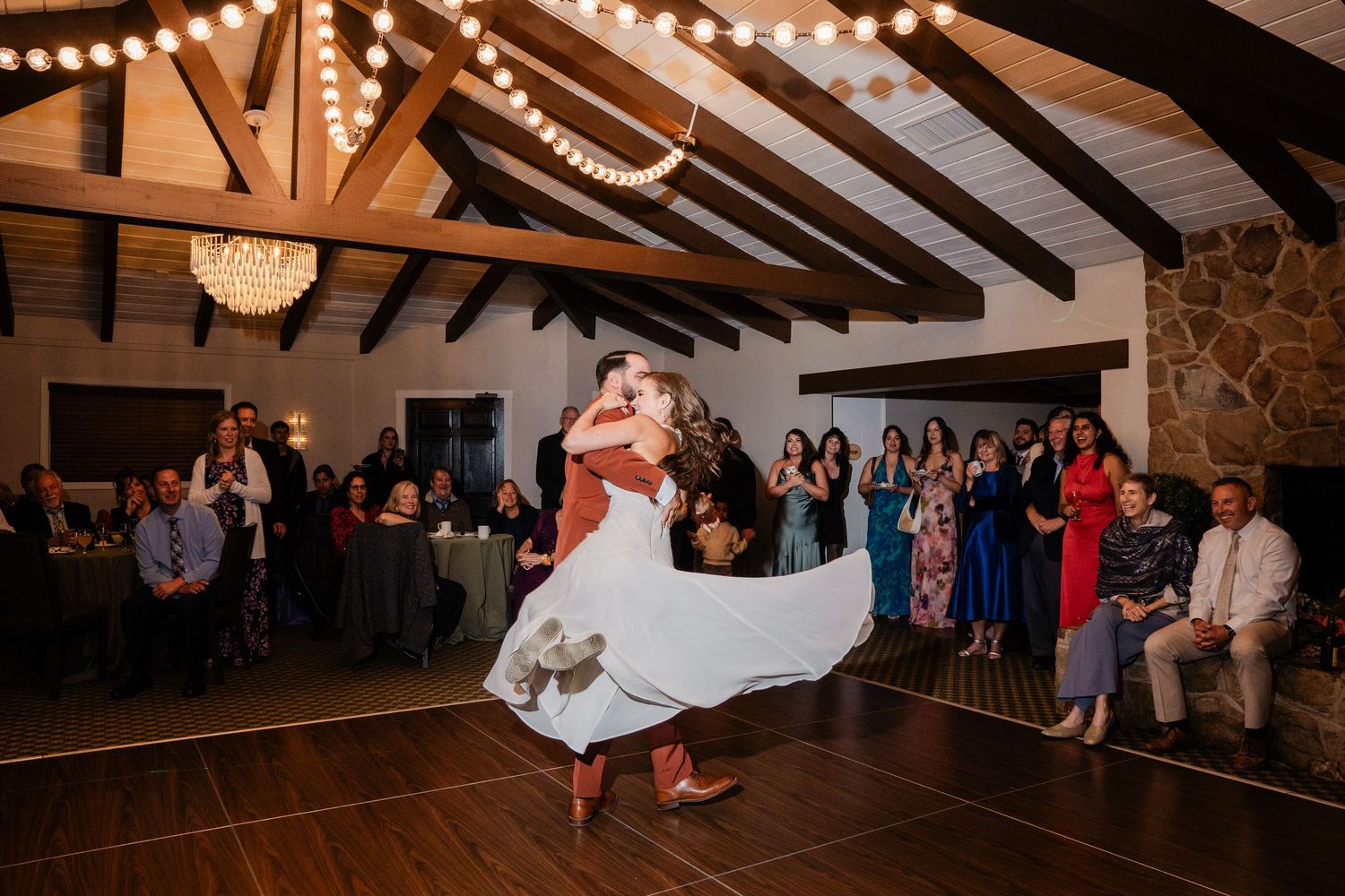 Groom lifts and spins bride in white dress on dance floor at wedding reception.