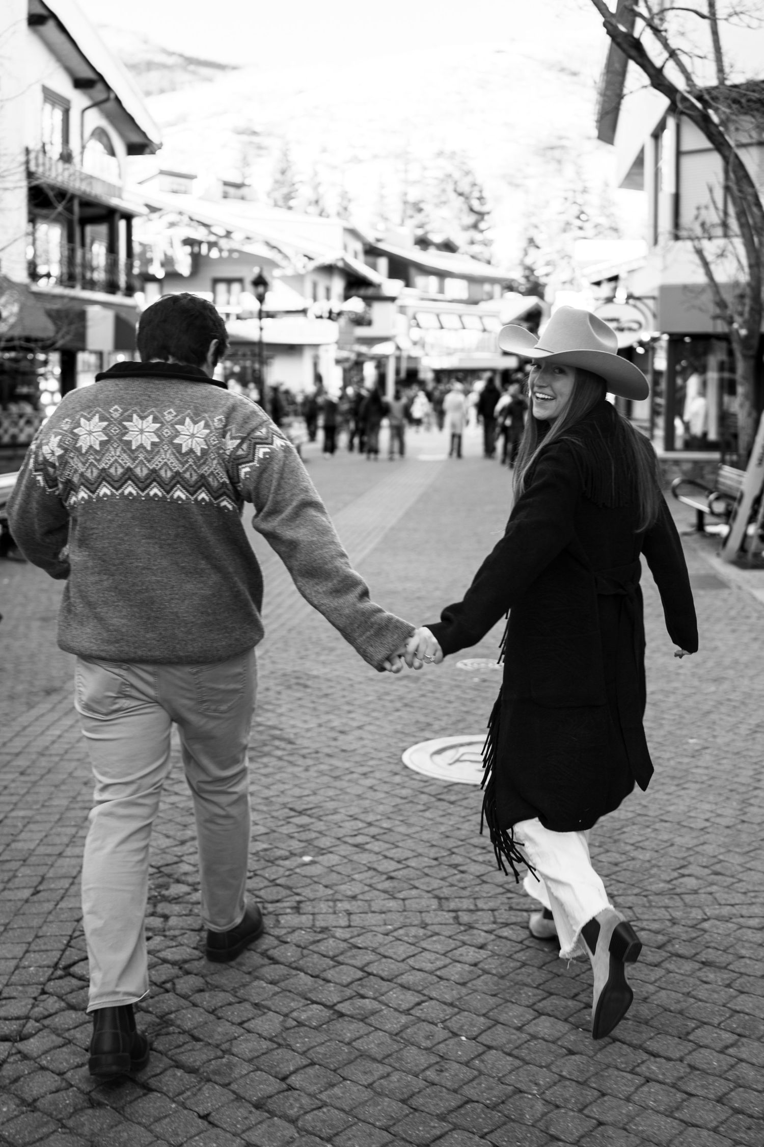 Black and white photo of couple holding hands walking through a charming winter ski town.