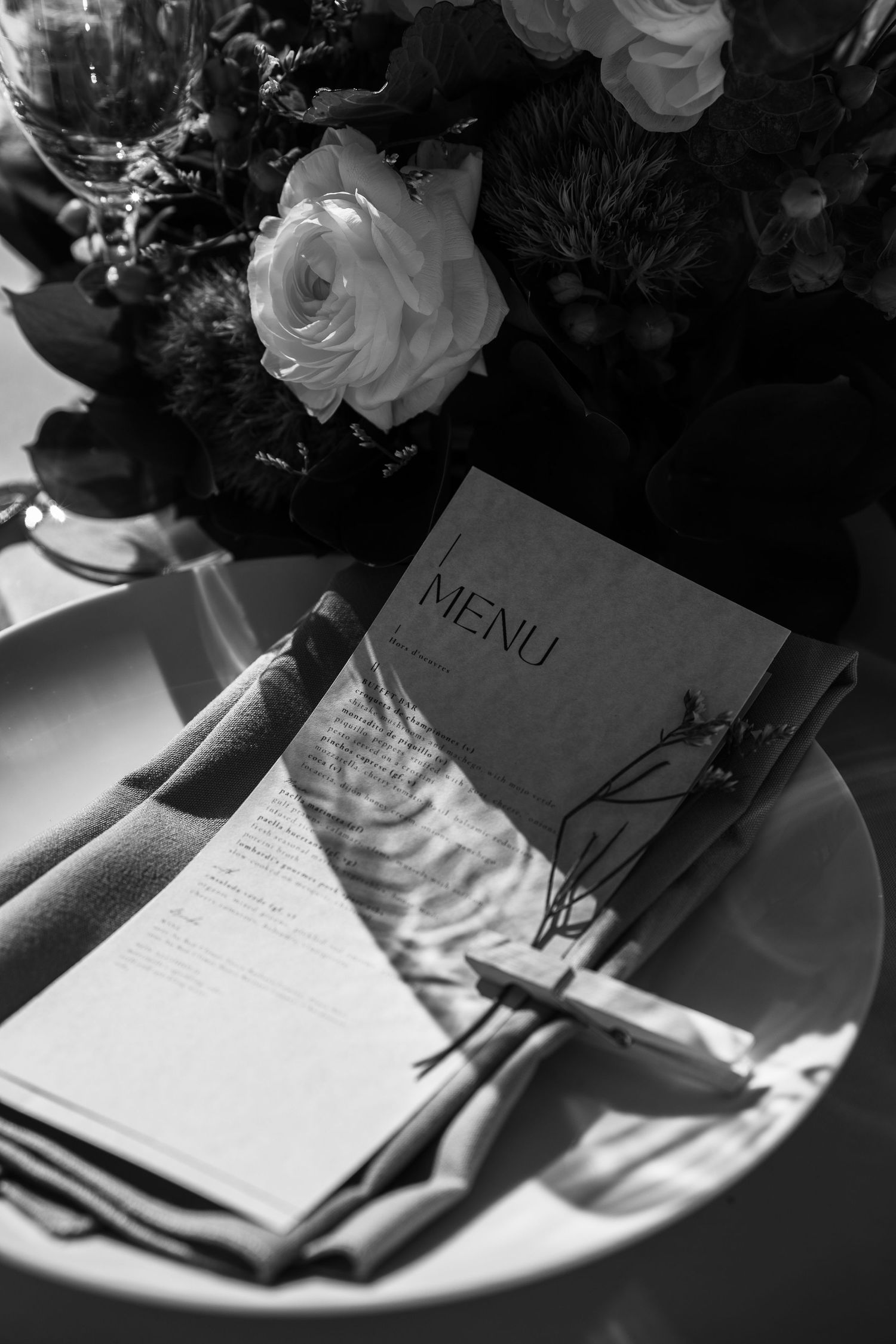 Black and white overhead shot of elegant wedding place setting with menu card and white roses.