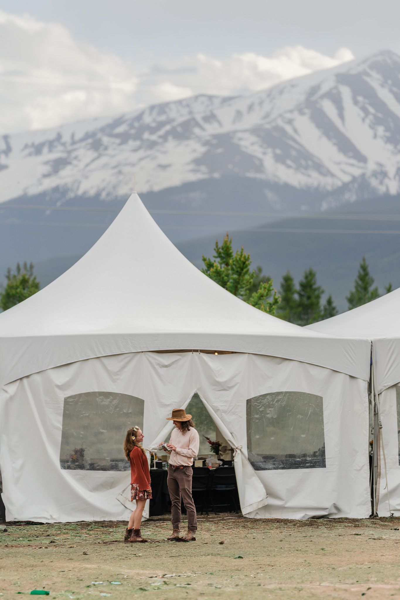 Couple shares a moment outside a white event tent with stunning snow-capped mountain backdrop at outdoor wedding.