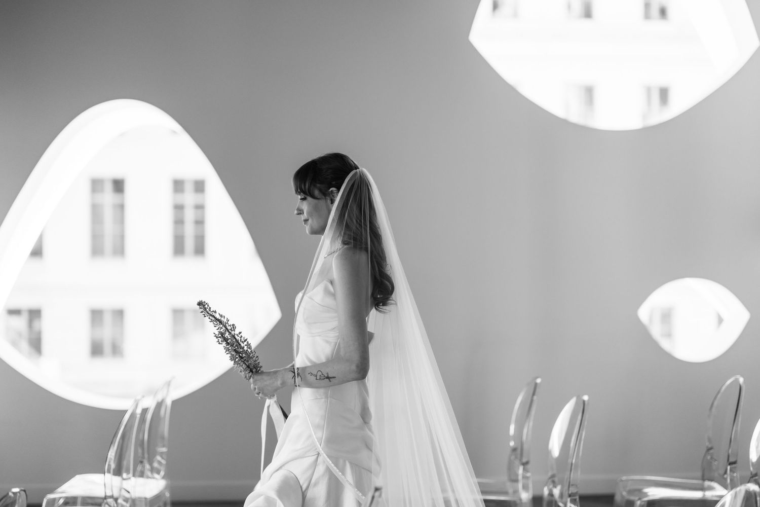 Bride in white gown and veil holds bouquet in elegant black and white wedding photo with soft lighting.
