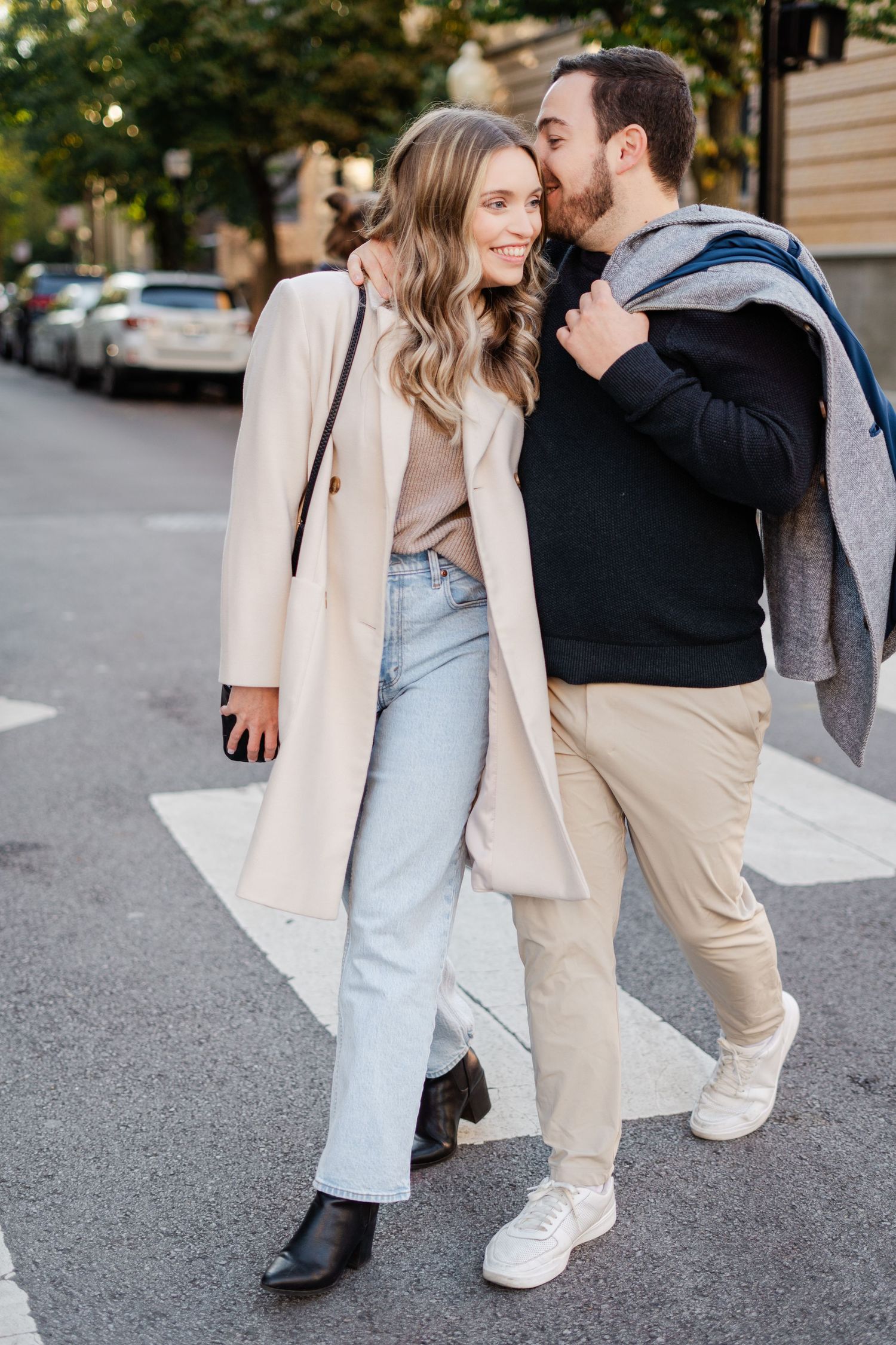Happy engaged couple walking together across a city street, man kissing woman on the cheek.